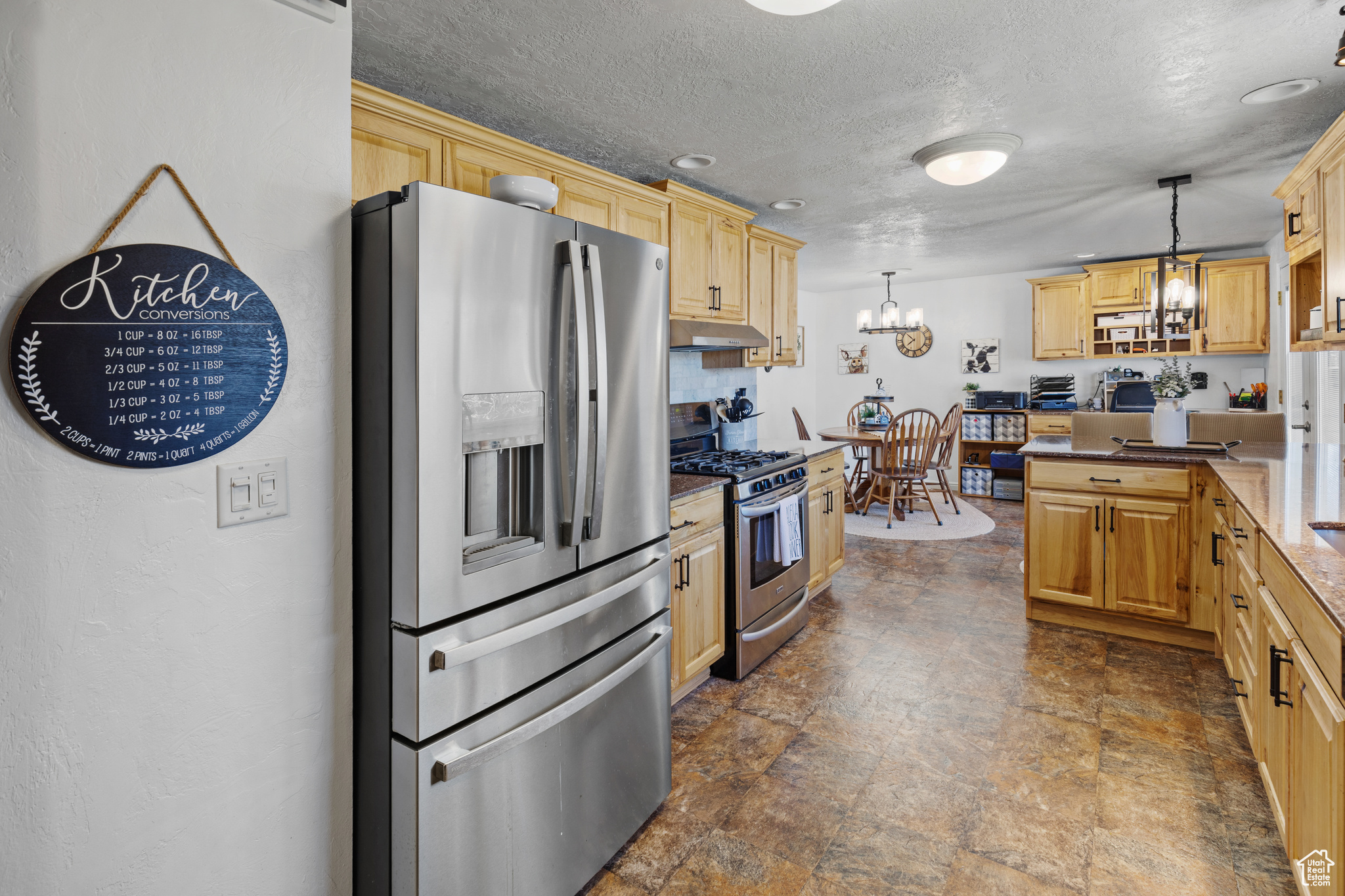 Kitchen with an inviting chandelier, appliances with stainless steel finishes, dark tile floors, a textured ceiling, and pendant lighting