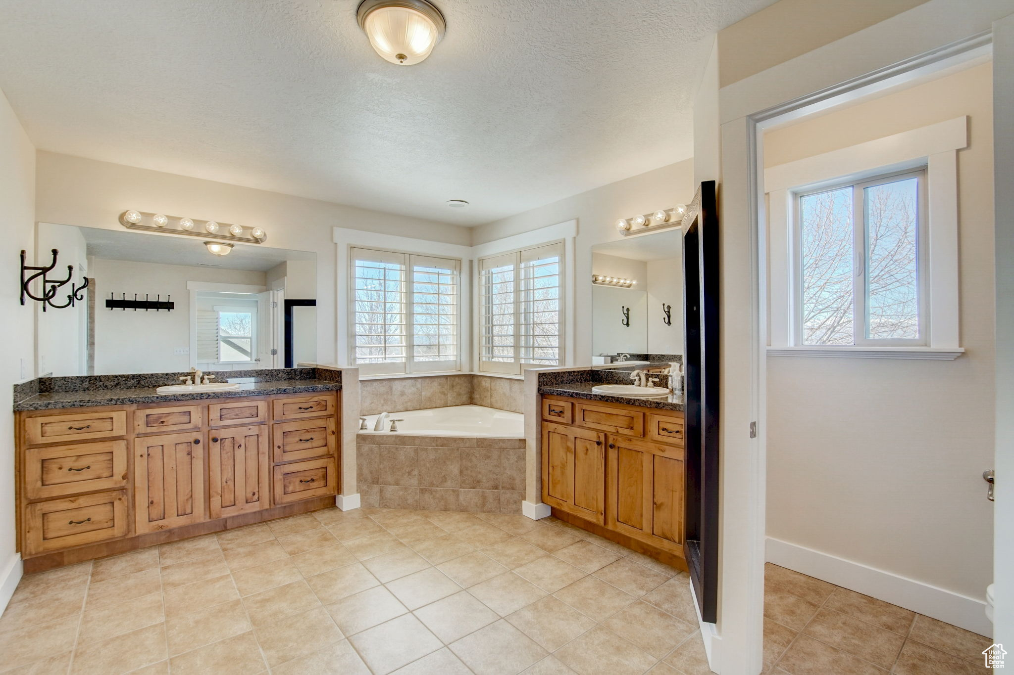 Bathroom featuring a relaxing tiled bath, tile floors, plenty of natural light, and double vanity