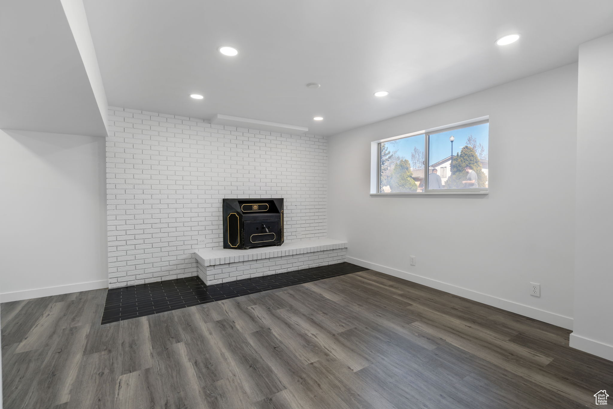 Unfurnished living room featuring dark hardwood / wood-style floors, brick wall, and a brick fireplace
