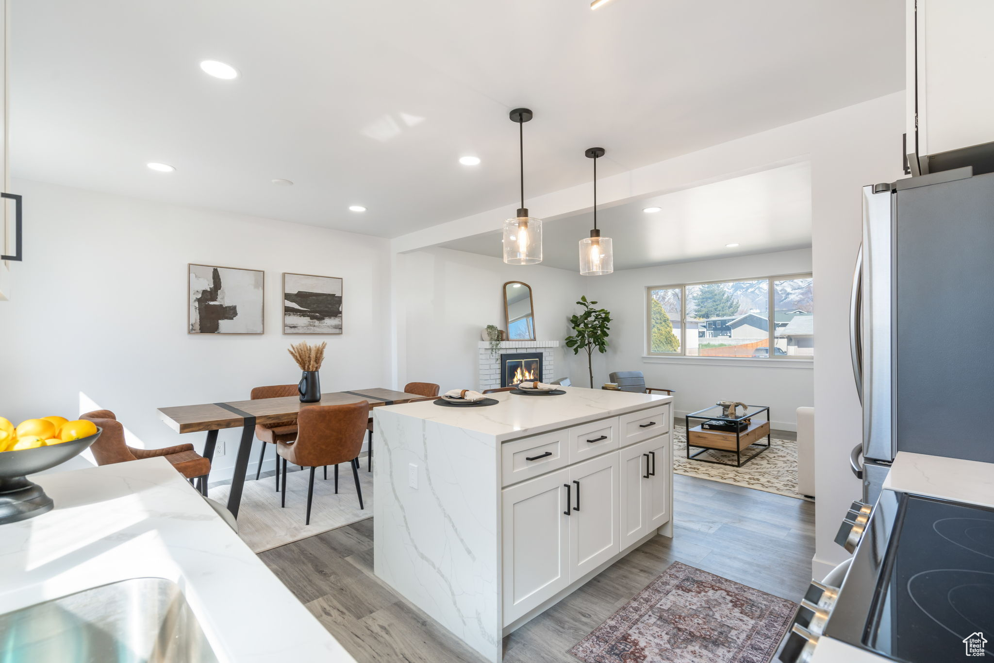 Kitchen featuring decorative light fixtures, light hardwood / wood-style floors, white cabinets, stainless steel fridge, and a fireplace