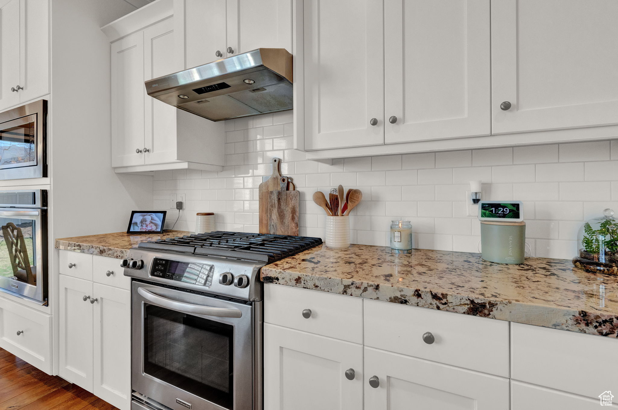 Kitchen with tasteful backsplash, light hardwood / wood-style flooring, appliances with stainless steel finishes, white cabinets, and light stone counters