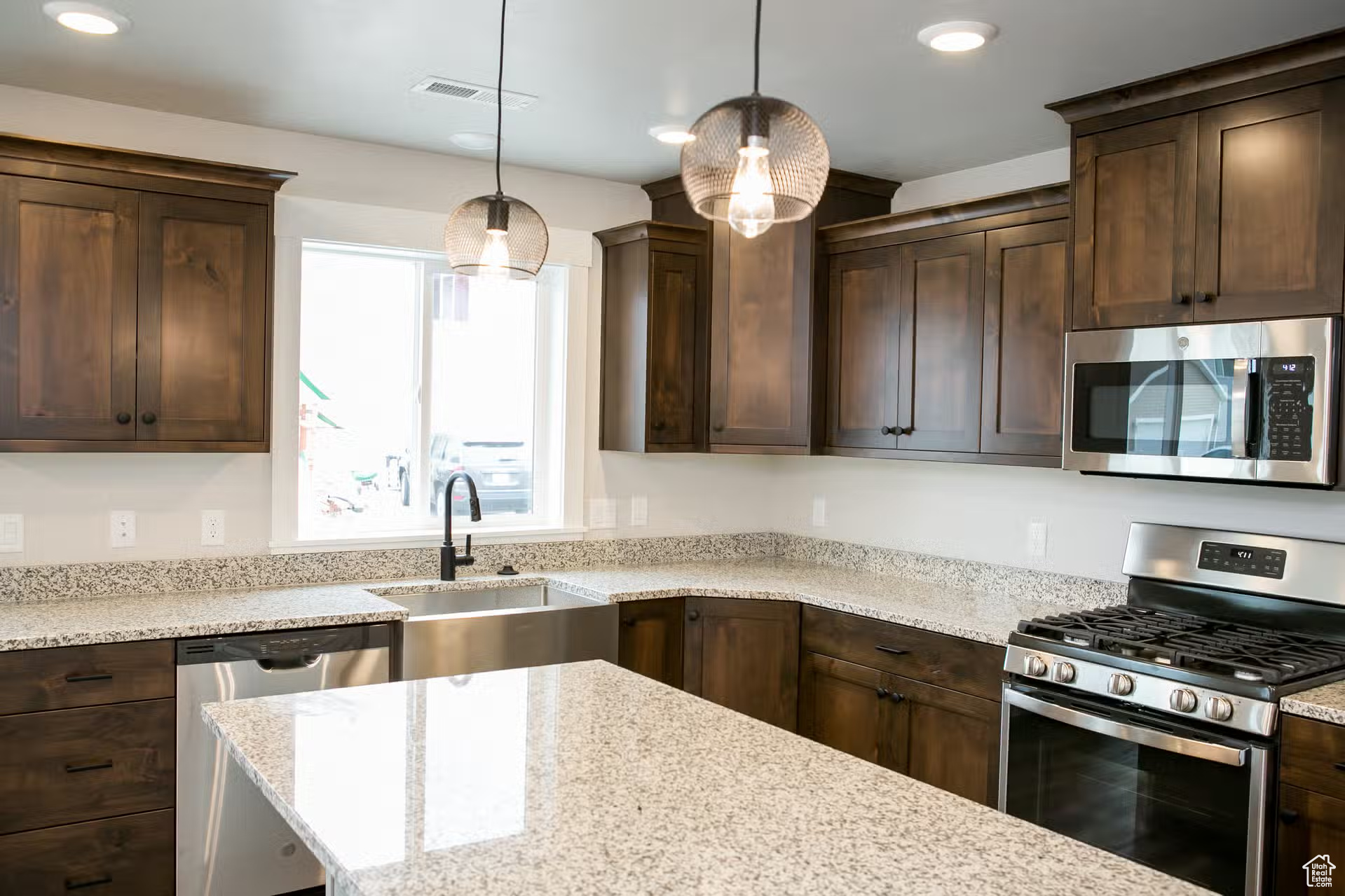 Kitchen featuring appliances with stainless steel finishes, pendant lighting, sink, dark brown cabinets, and light stone countertops