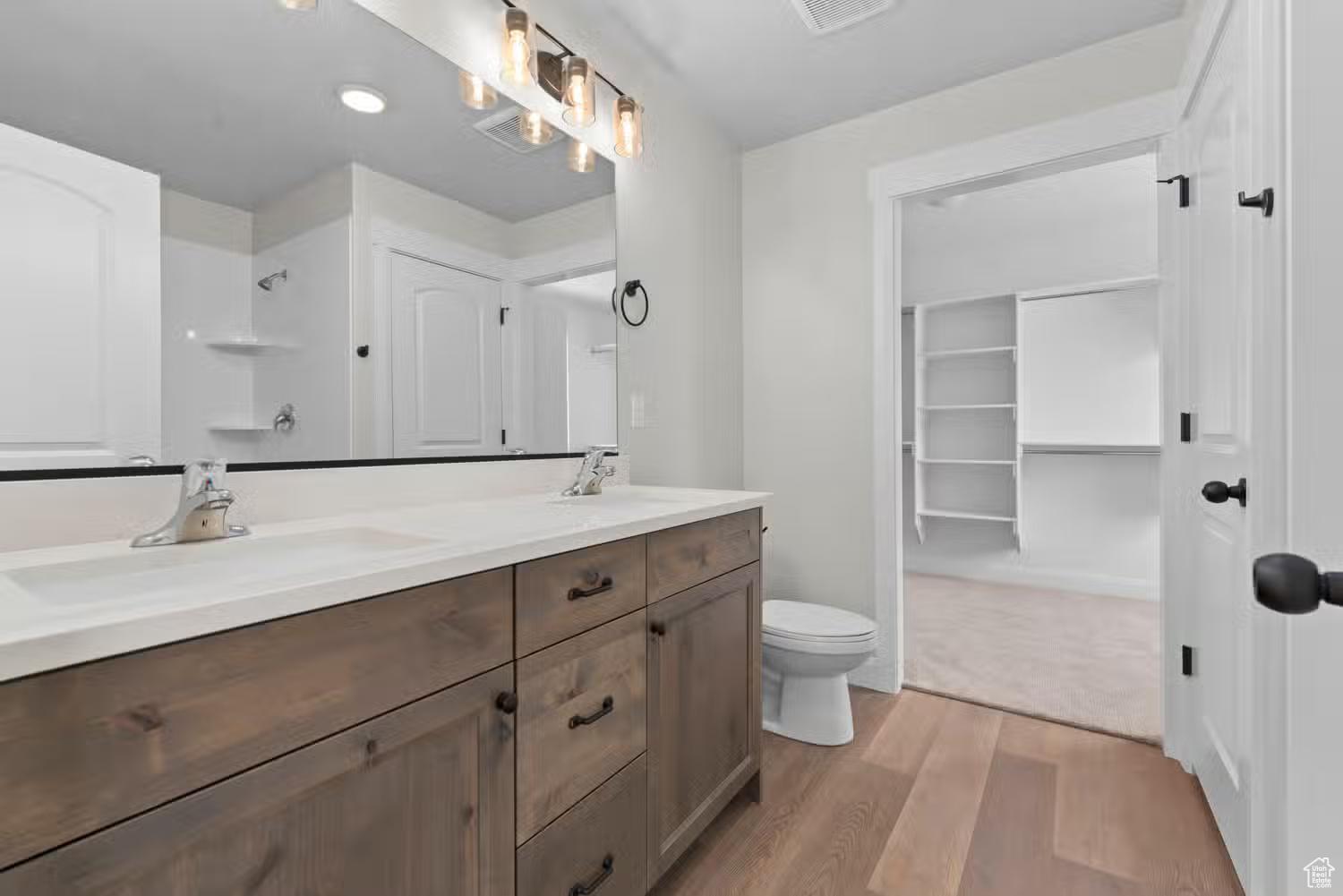 Bathroom featuring large vanity, dual sinks, toilet, and wood-type flooring