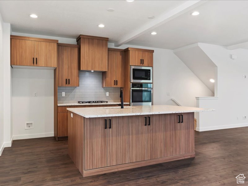 Kitchen featuring appliances with stainless steel finishes, tasteful backsplash, dark wood-type flooring, a breakfast bar area, and a center island with sink