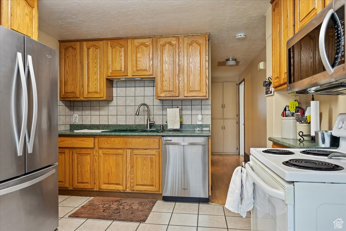 Kitchen featuring tasteful backsplash, light tile floors, stainless steel appliances, a textured ceiling, and sink