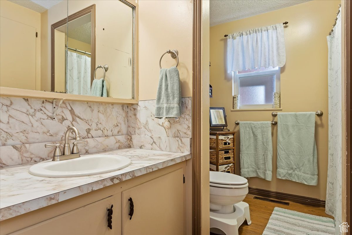 Bathroom featuring toilet, backsplash, oversized vanity, a textured ceiling, and hardwood / wood-style flooring