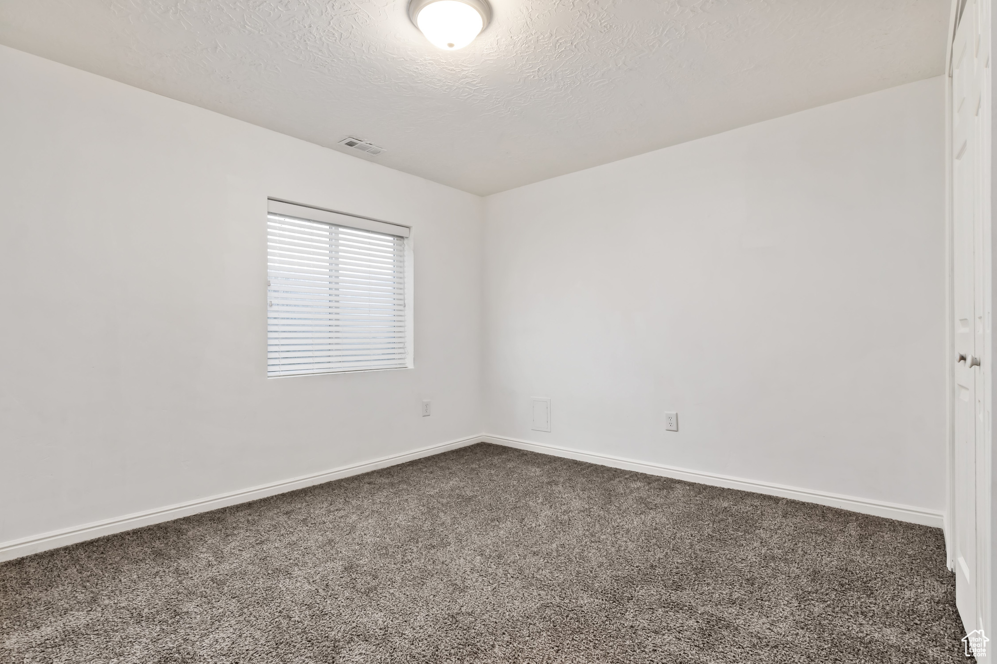 Unfurnished room featuring a textured ceiling and dark carpet