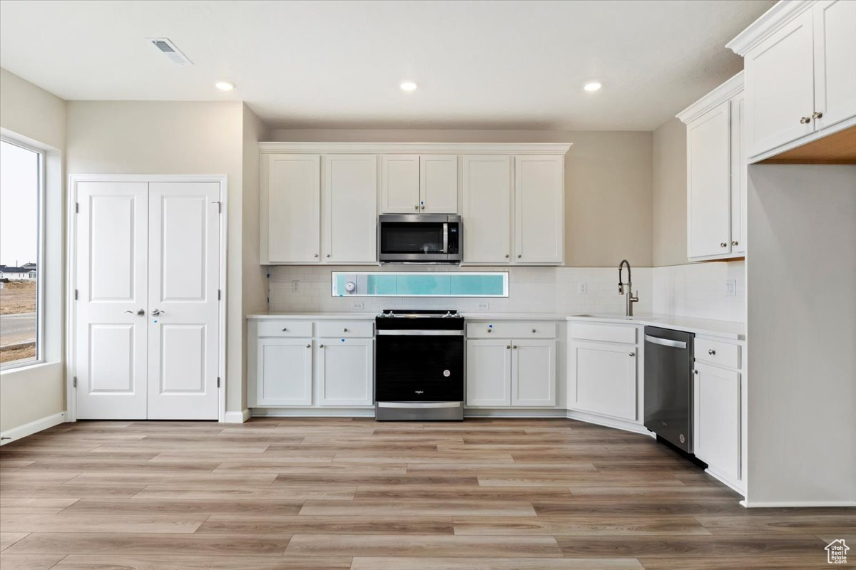 Kitchen with white cabinets, appliances with stainless steel finishes, sink, tasteful backsplash, and light hardwood / wood-style floors