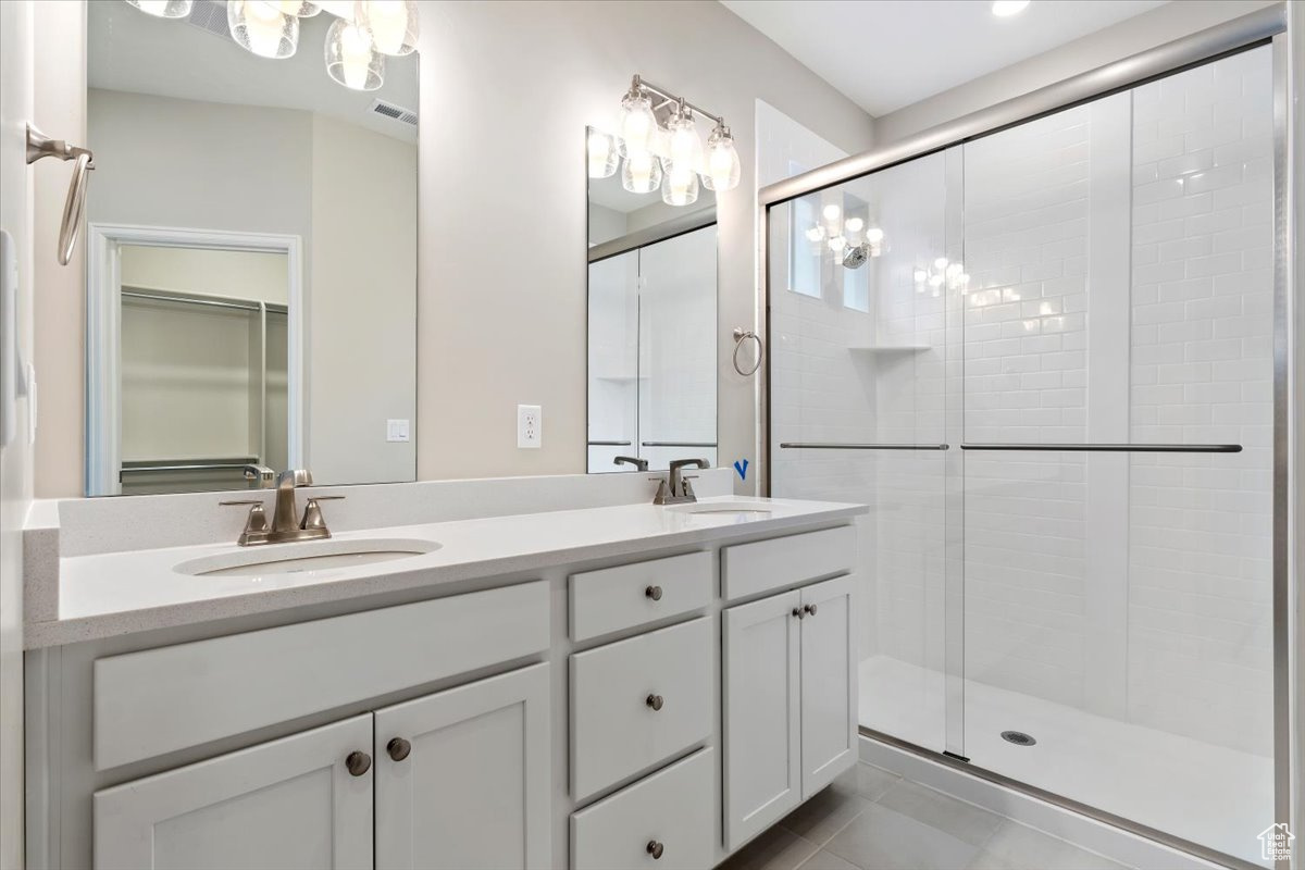 Bathroom with tile flooring, walk in shower, dual vanity, and an inviting chandelier