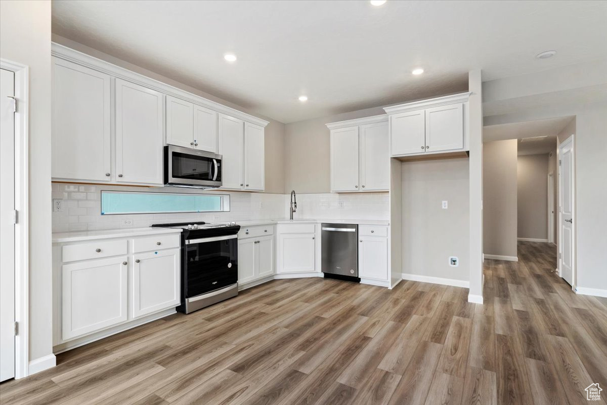 Kitchen featuring backsplash, stainless steel appliances, light hardwood / wood-style floors, and white cabinetry