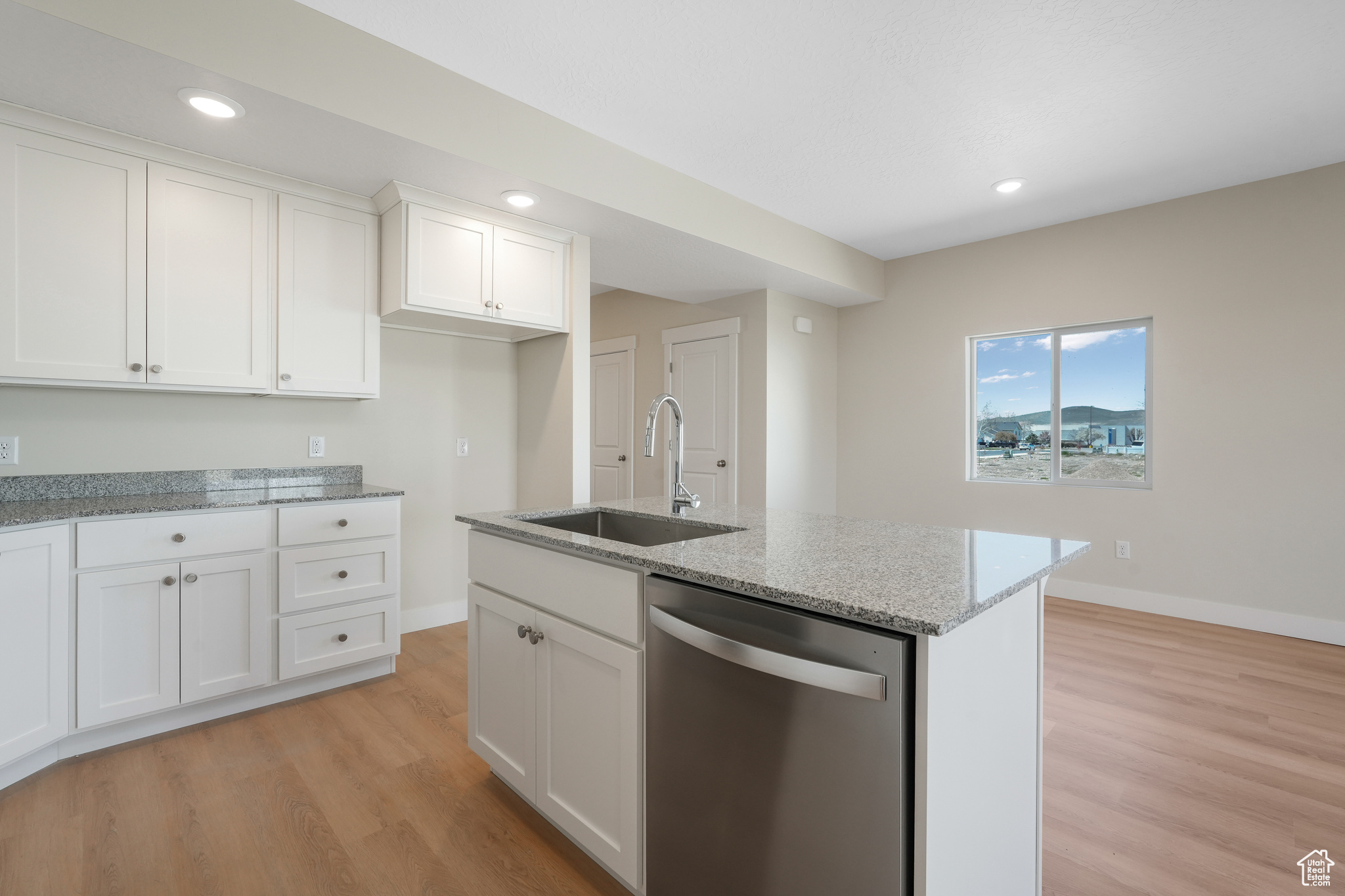 Kitchen with a kitchen island with sink, light stone countertops, light hardwood / wood-style flooring, white cabinetry, and dishwasher