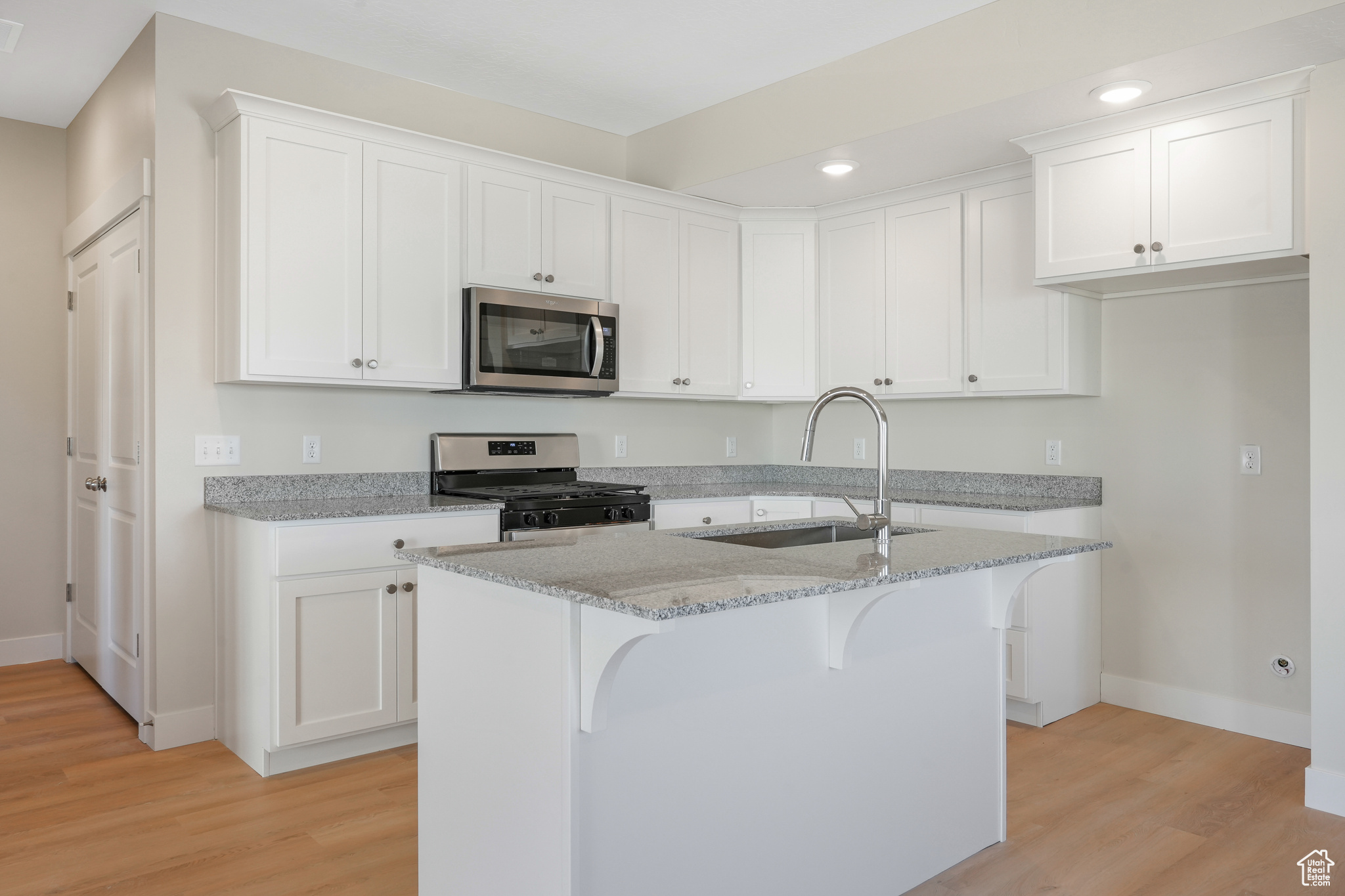 Kitchen with white cabinets, appliances with stainless steel finishes, light hardwood / wood-style flooring, and light stone countertops