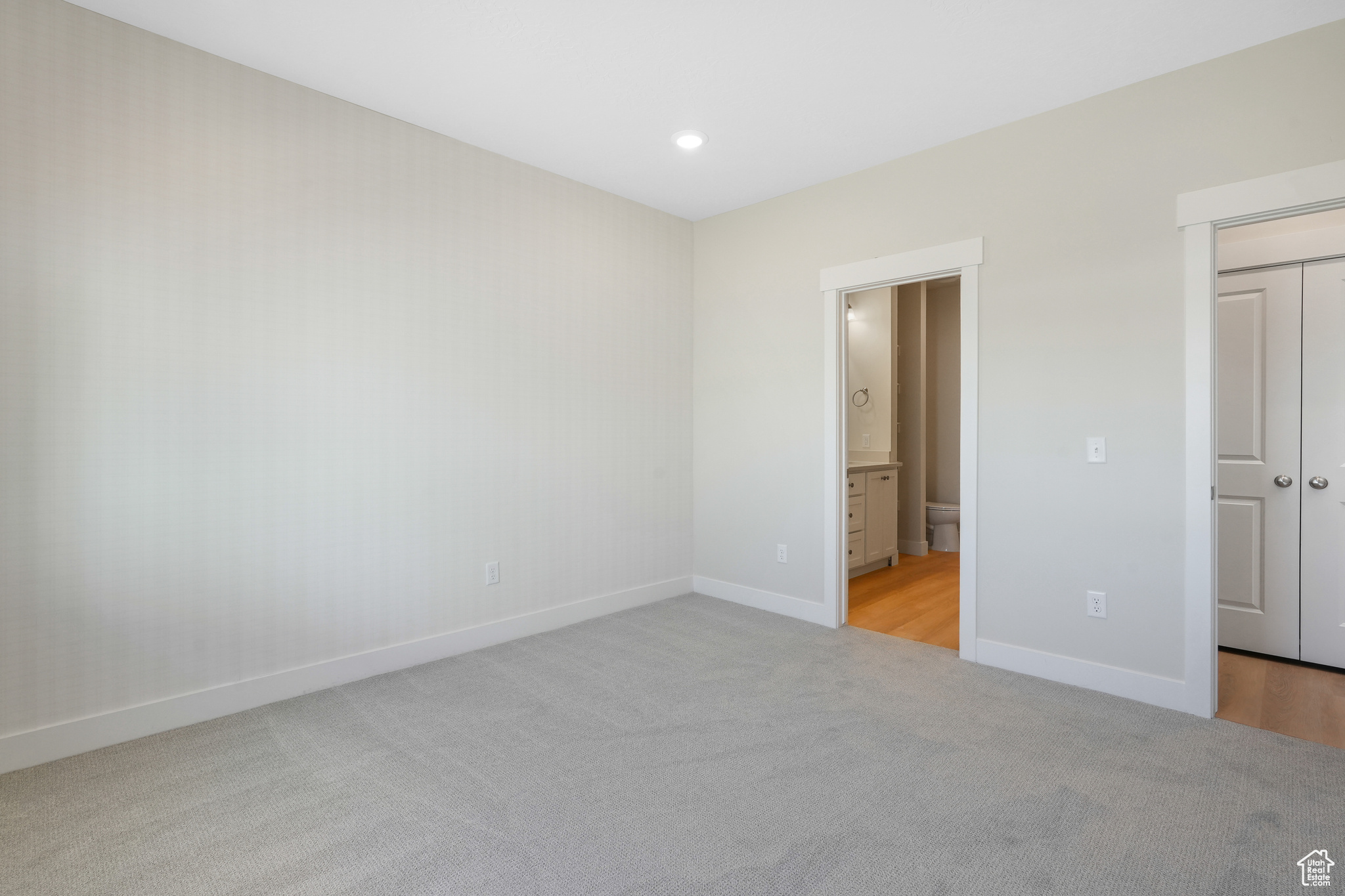 Unfurnished bedroom with light colored carpet and connected bathroom