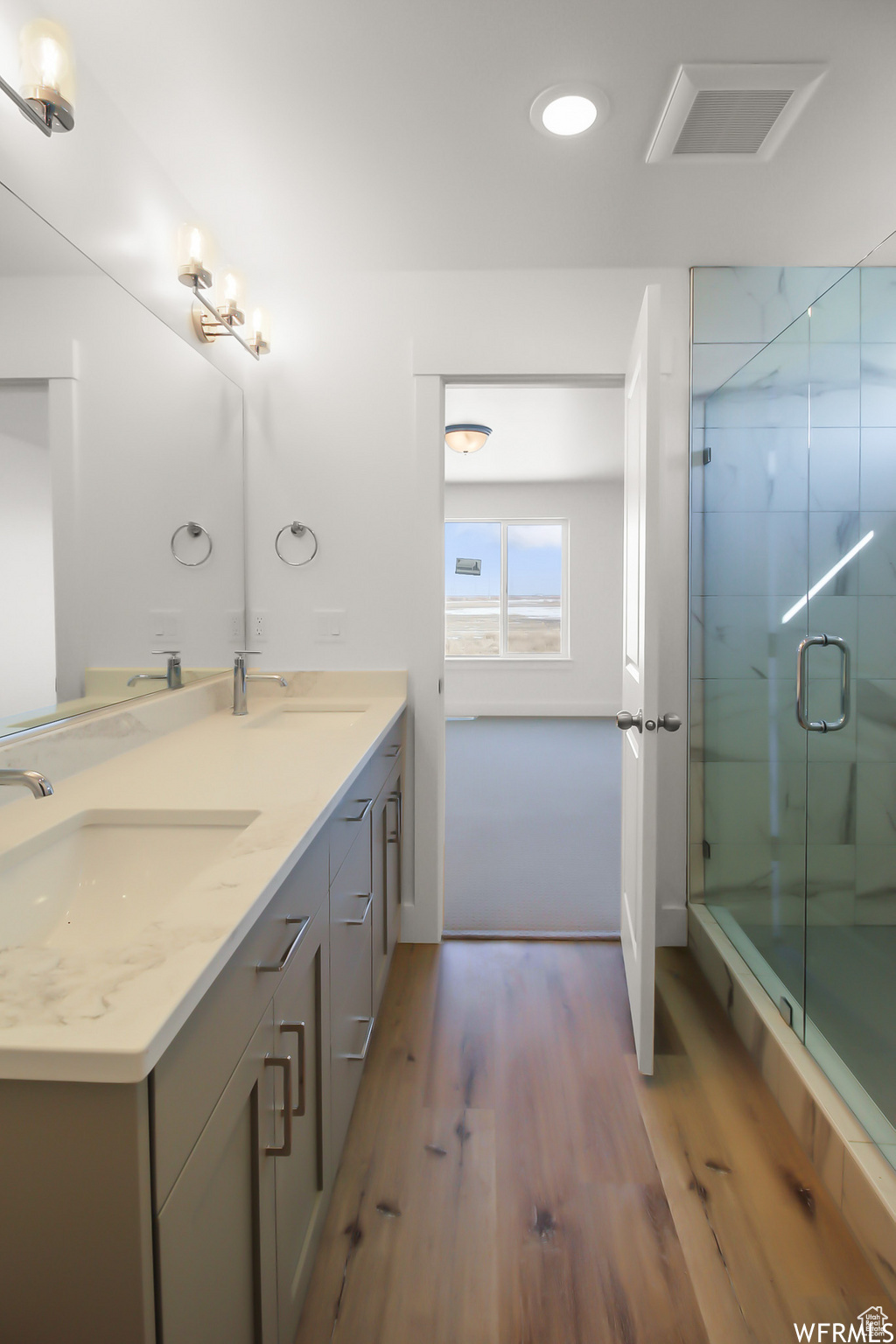 Bathroom featuring a shower with door, double vanity, and hardwood / wood-style flooring