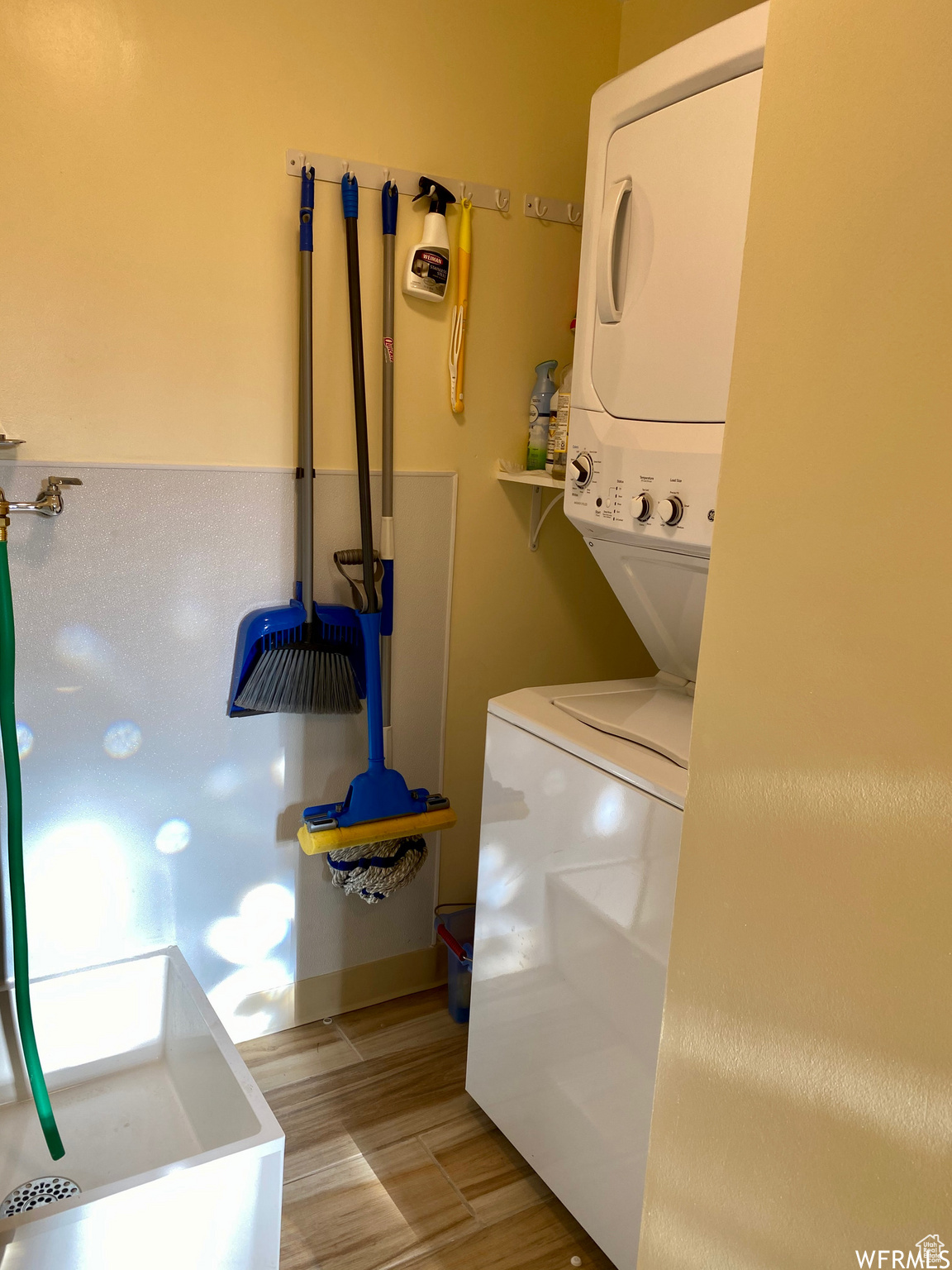 Laundry room with stacked washer and clothes dryer and light wood-type flooring