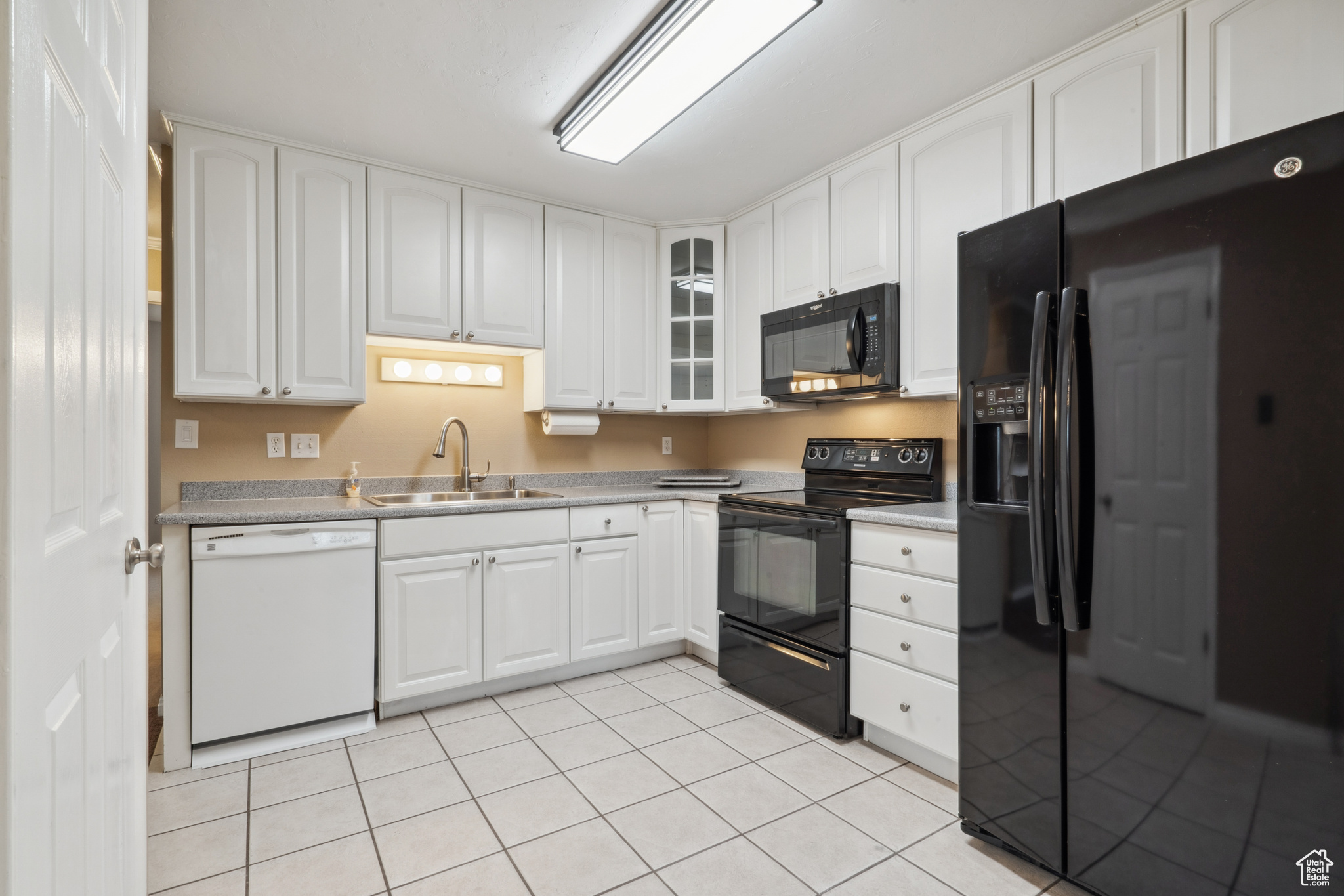 Kitchen featuring white cabinets, sink, light tile flooring, and black appliances