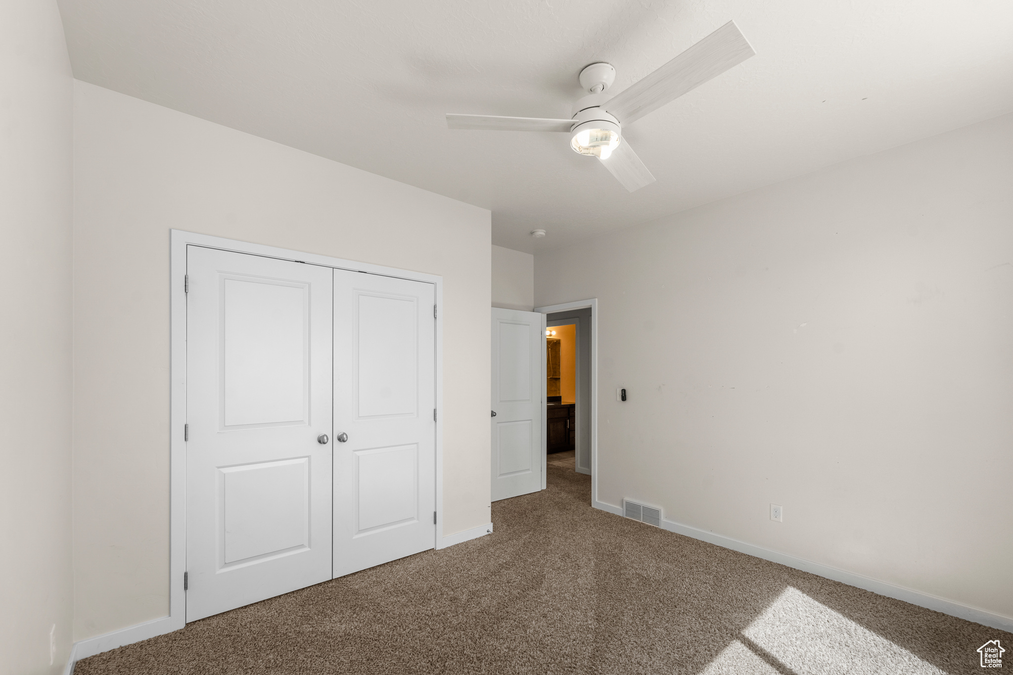 Unfurnished bedroom with ceiling fan, a closet, and dark colored carpet