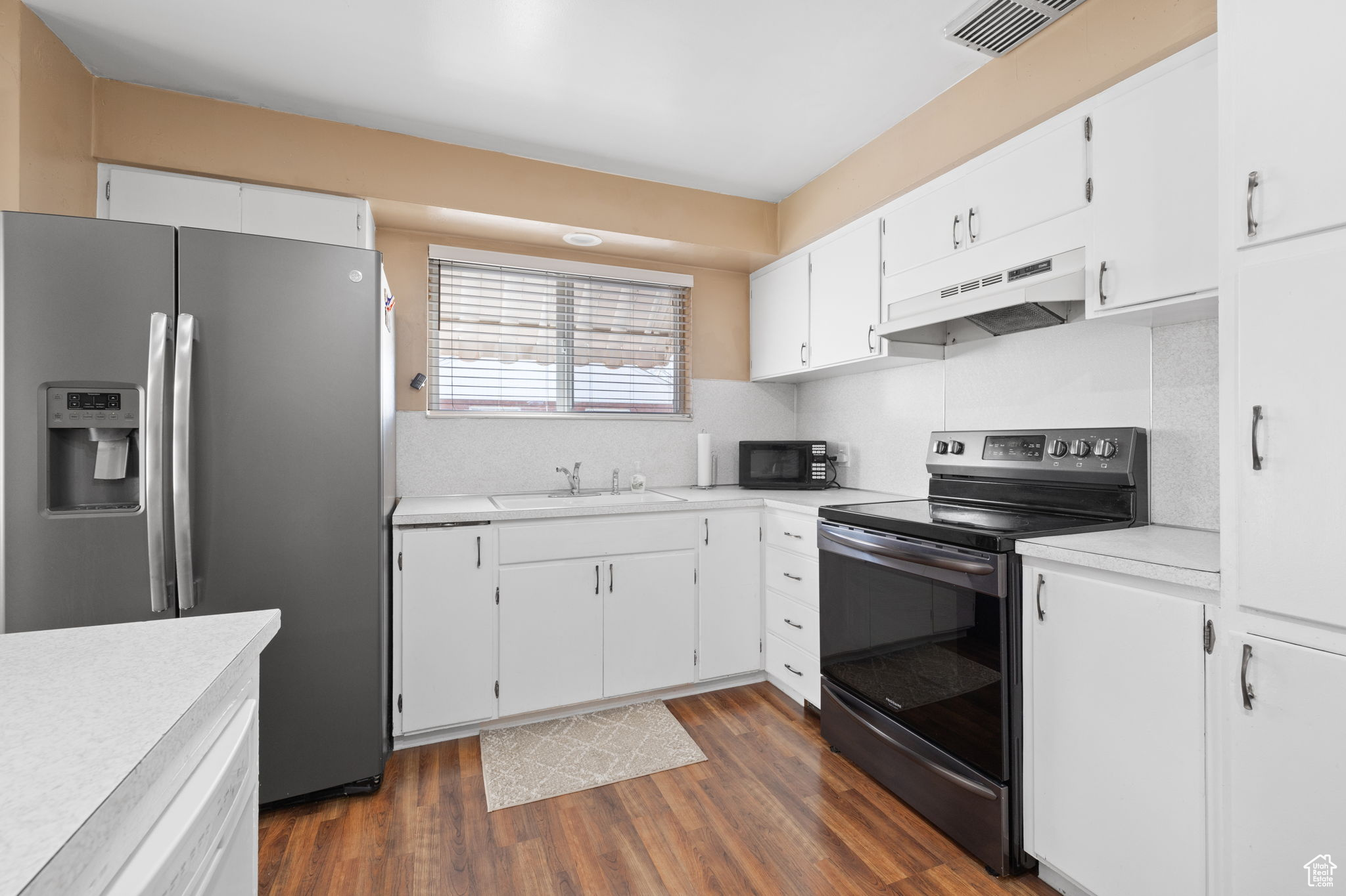 Kitchen with dark hardwood / wood-style floors, sink, backsplash, black appliances, and white cabinetry
