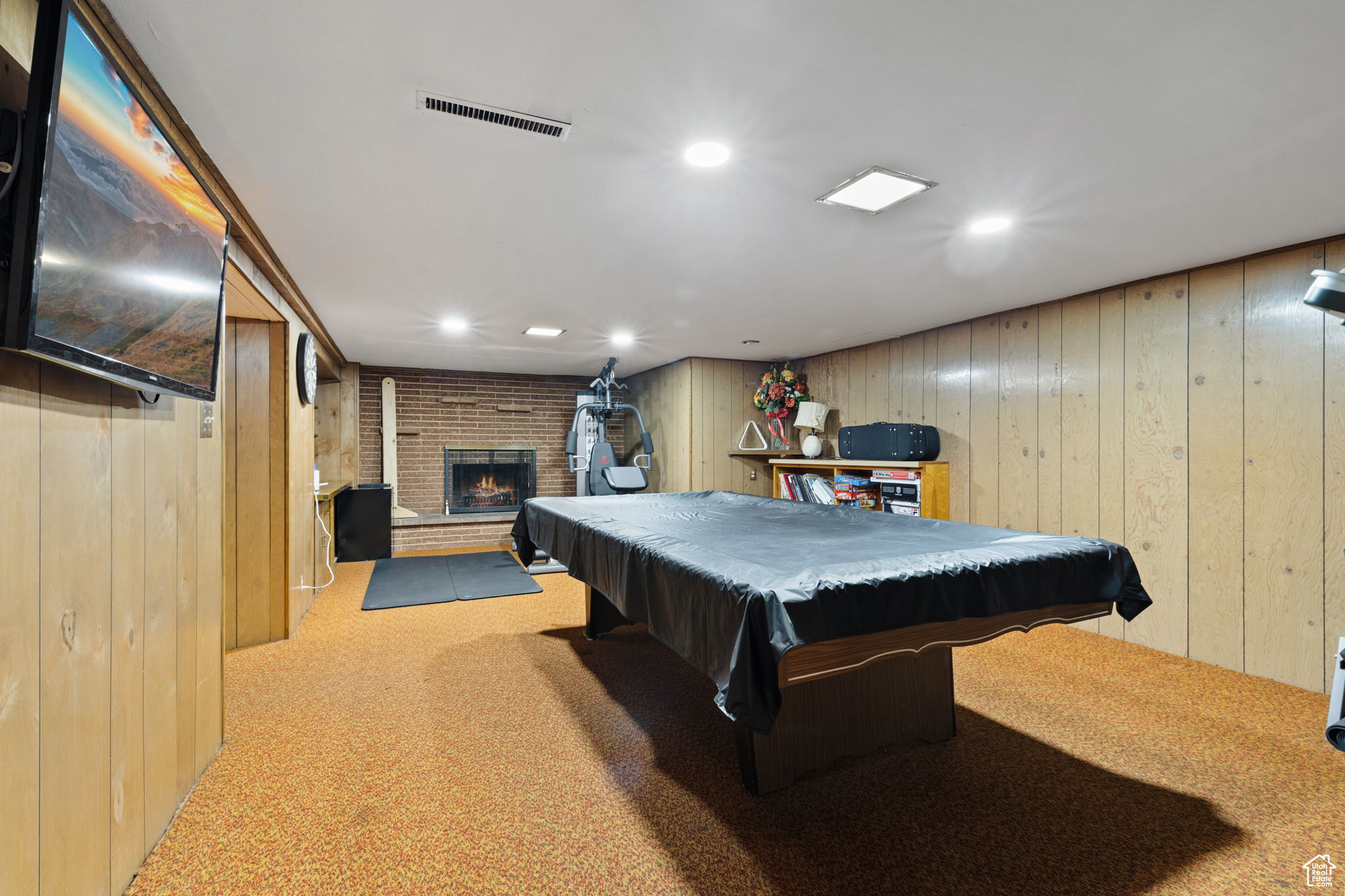 Game room featuring wooden walls, pool table, light carpet, and a brick fireplace