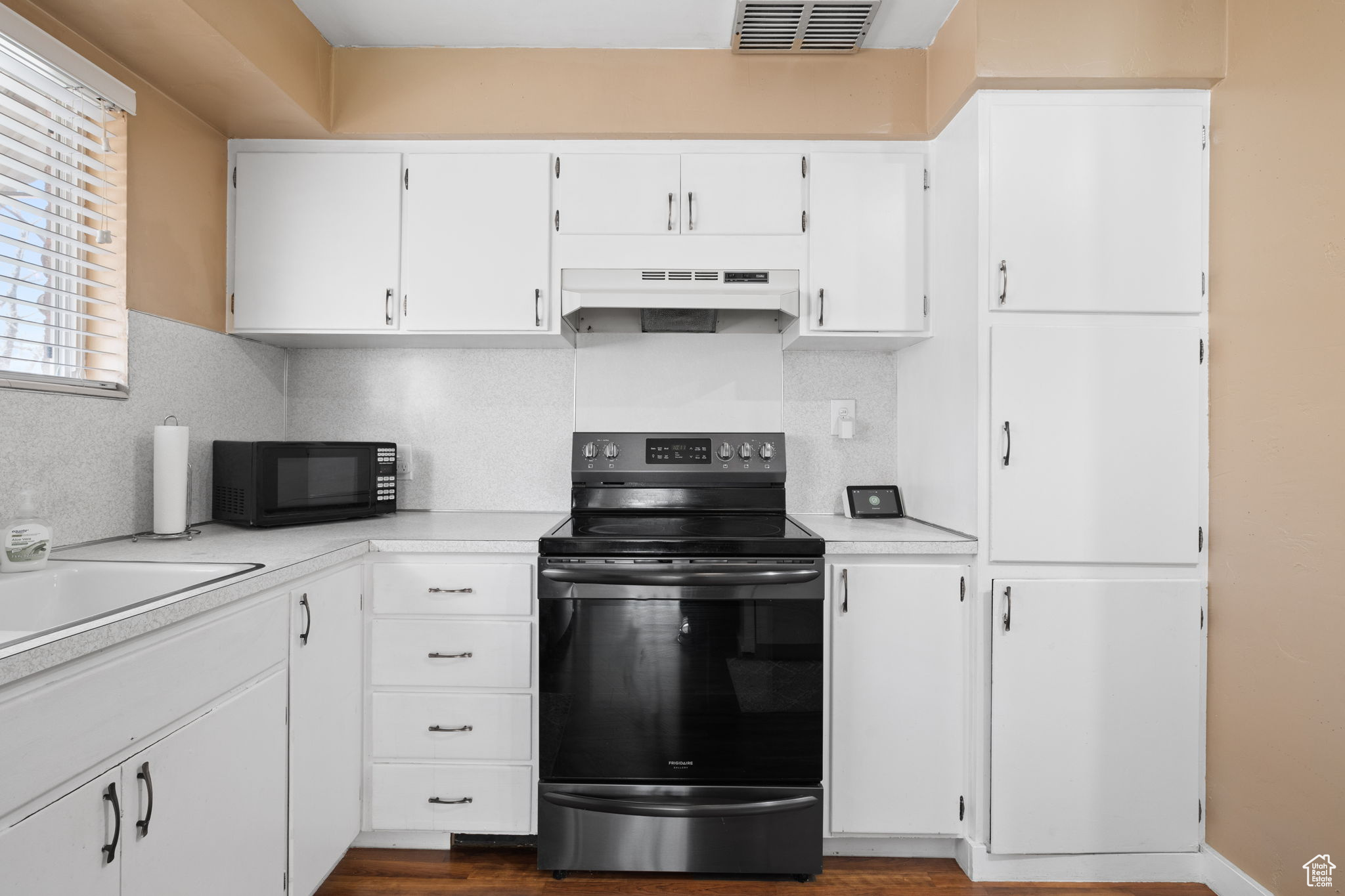 Kitchen with dark hardwood / wood-style floors, custom range hood, black appliances, and white cabinetry