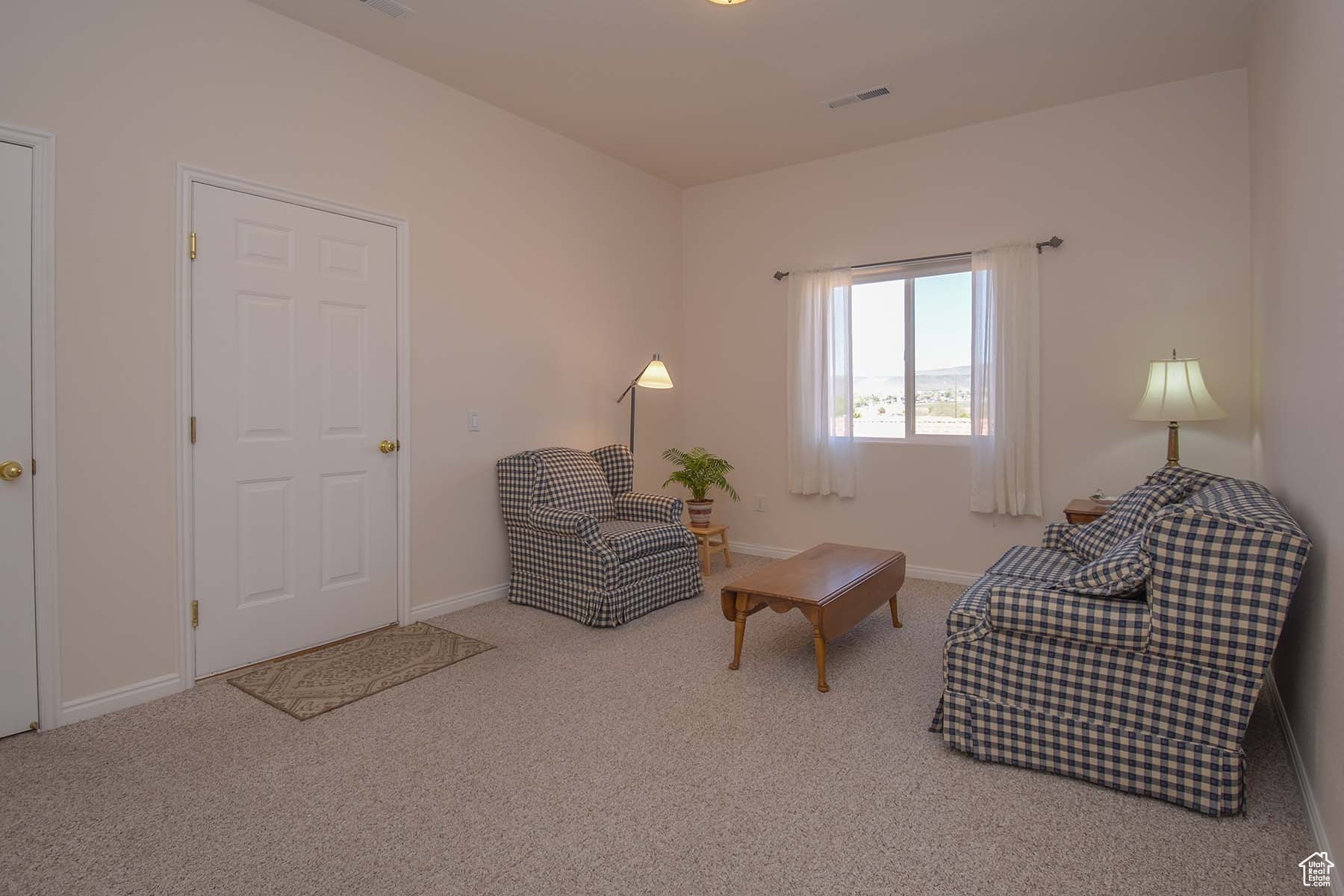 Sitting room with light colored carpet. Door leads to garage