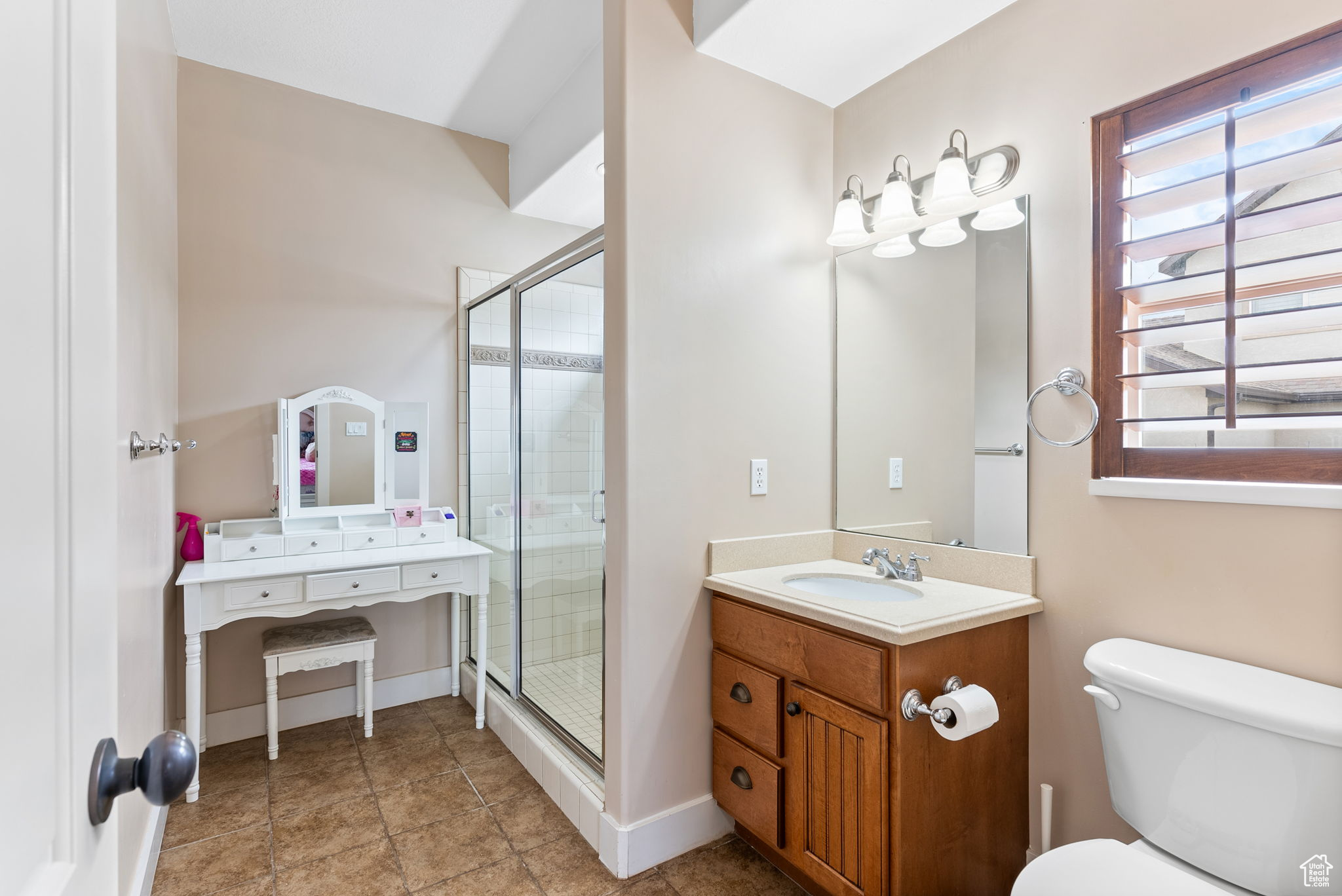 Bathroom featuring tile flooring, a shower with shower door, vanity with extensive cabinet space, and toilet