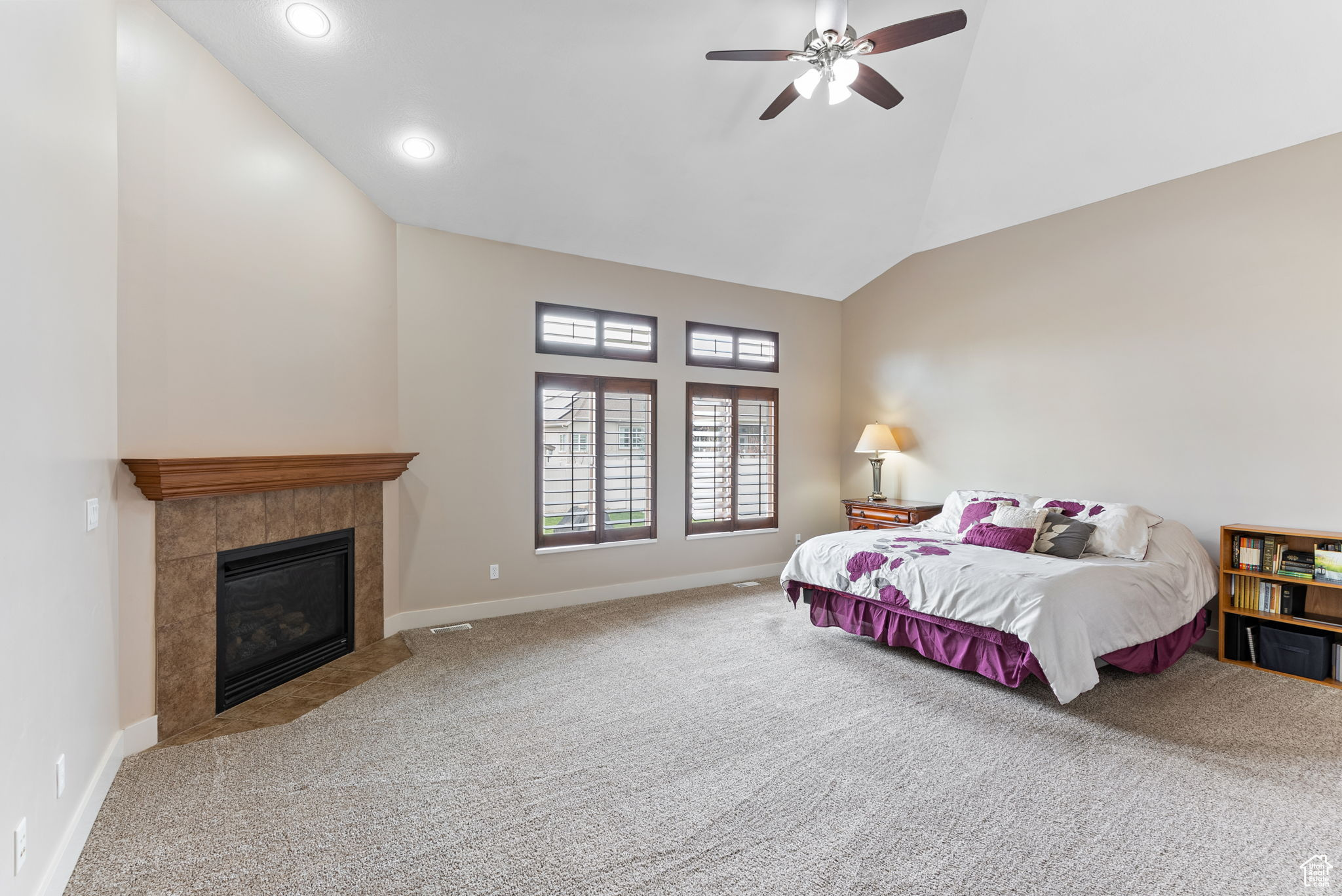 Carpeted bedroom featuring vaulted ceiling, ceiling fan, and a tile fireplace