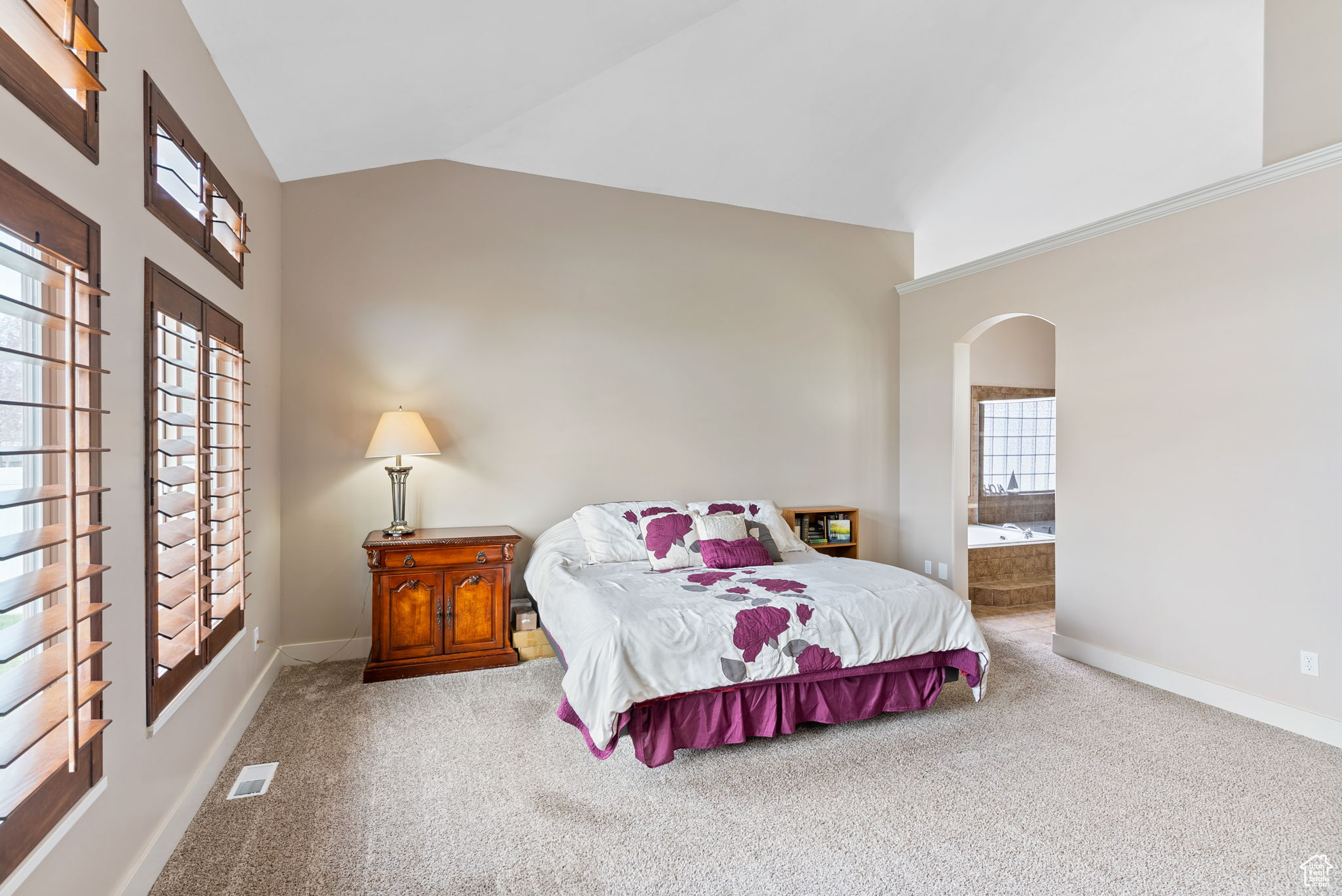Bedroom featuring light colored carpet, vaulted ceiling, and ensuite bath