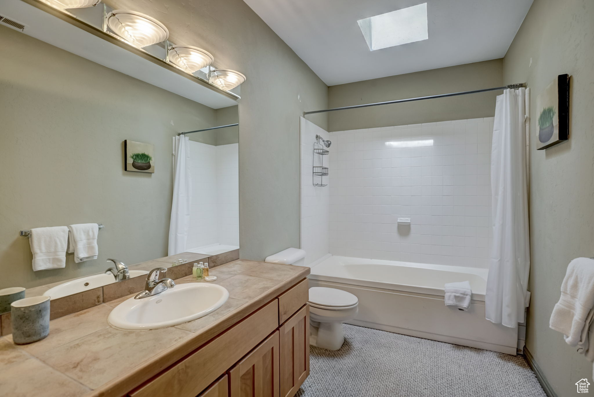 Full bathroom featuring toilet, shower / tub combo with curtain, vanity, and a skylight