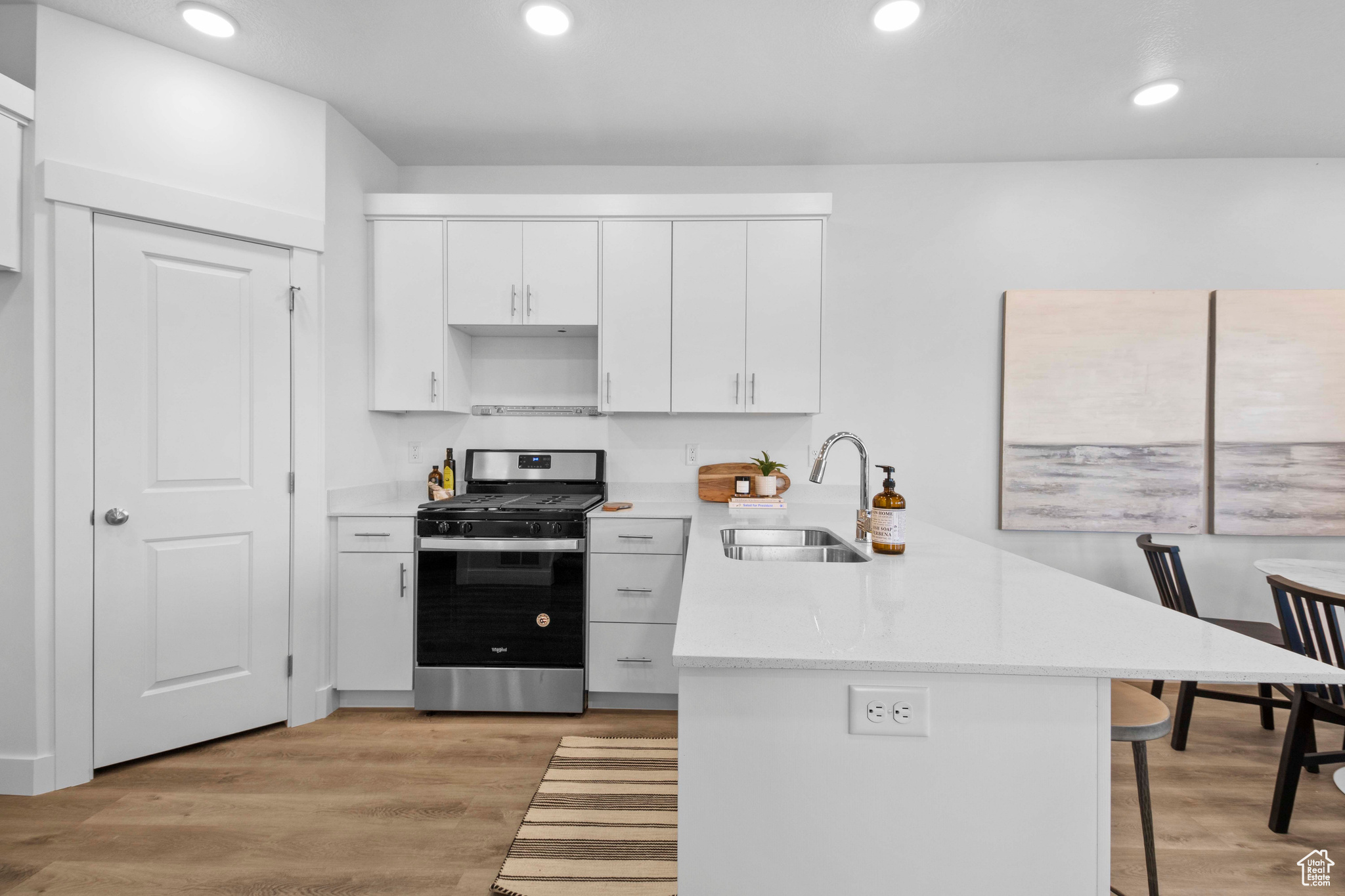 Kitchen with light hardwood / wood-style flooring, a breakfast bar area, white cabinetry, gas stove, and sink