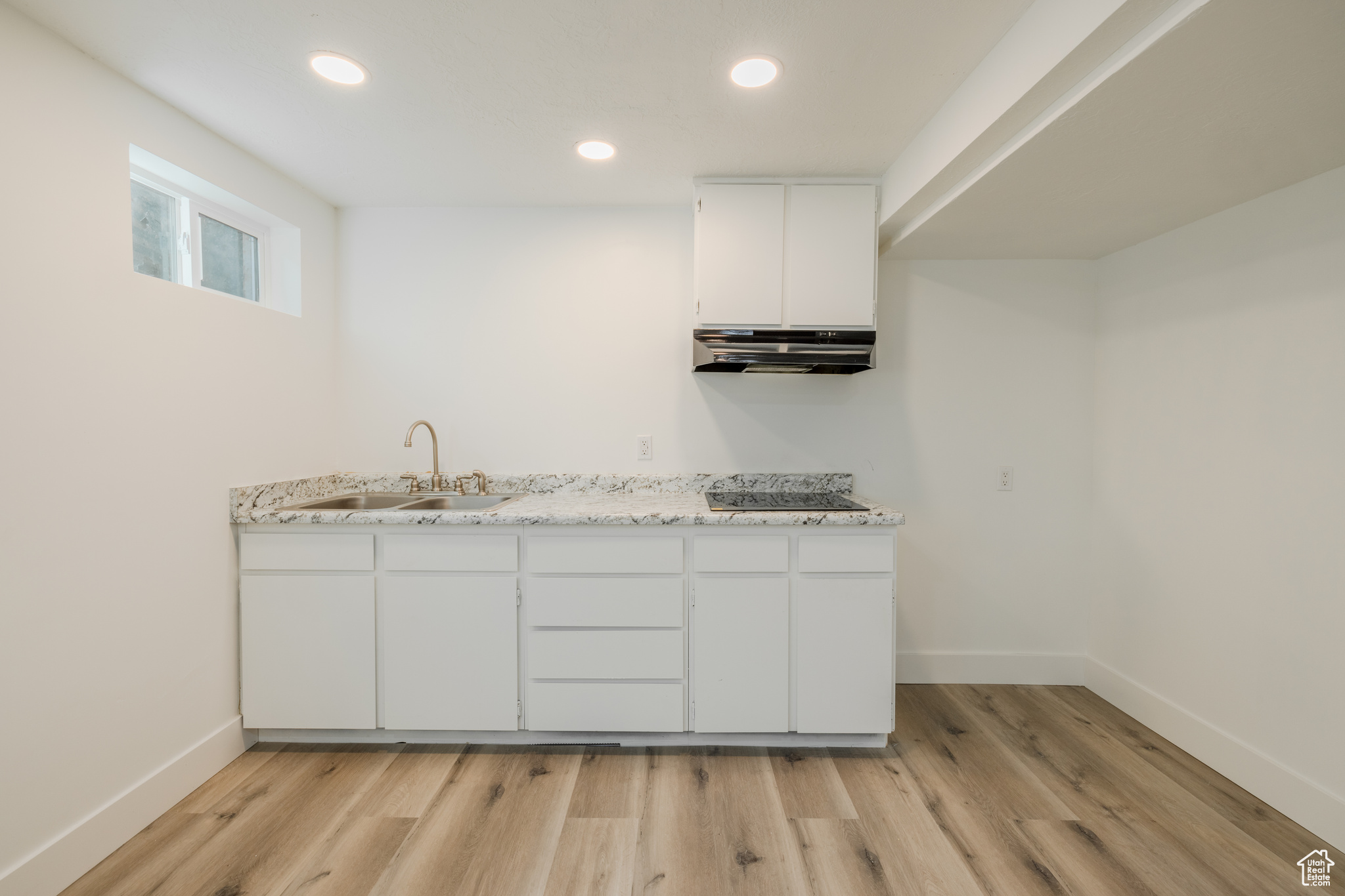 Kitchen featuring light stone countertops, range hood, light hardwood / wood-style floors, sink, and white cabinets