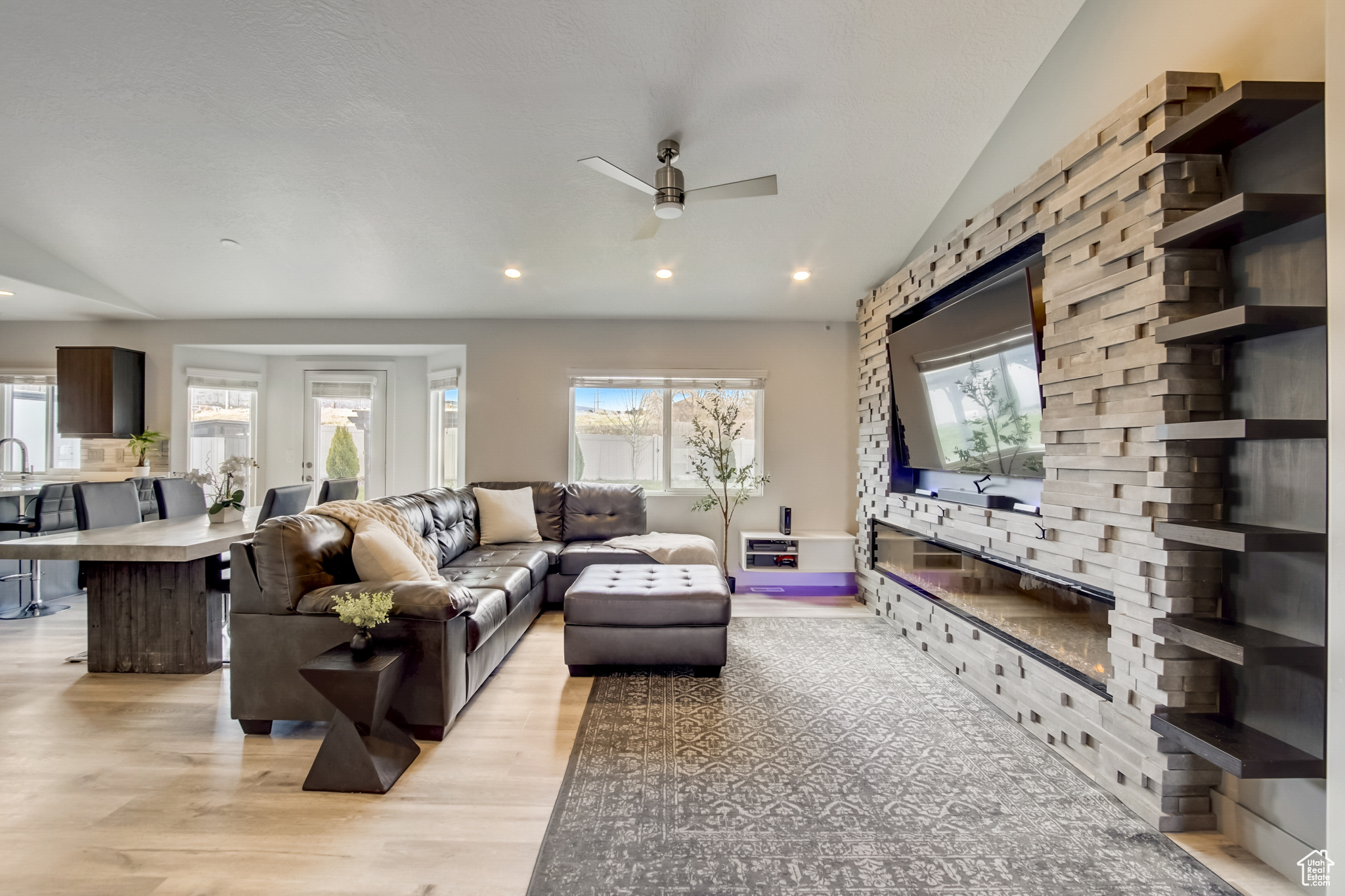 Living room featuring lofted ceiling, ceiling fan, a wealth of natural light, and light hardwood / wood-style flooring