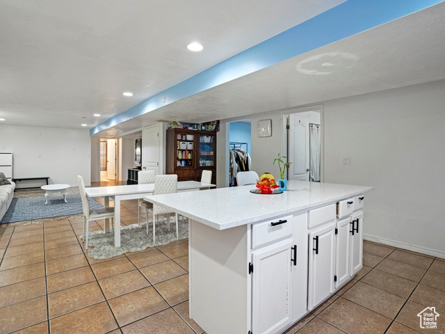 Kitchen featuring white cabinets, a kitchen island, light stone counters, and light tile flooring