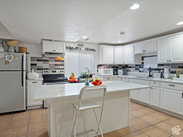 Kitchen with a kitchen island, white appliances, white cabinetry, and light tile floors