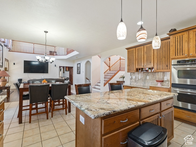 Kitchen with decorative light fixtures, an inviting chandelier, tasteful backsplash, a center island with sink, and double oven
