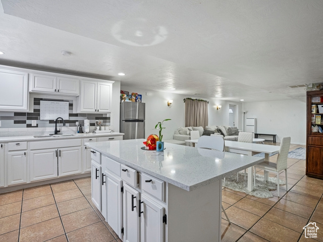 Kitchen featuring stainless steel refrigerator, a center island, light tile floors, and white cabinets