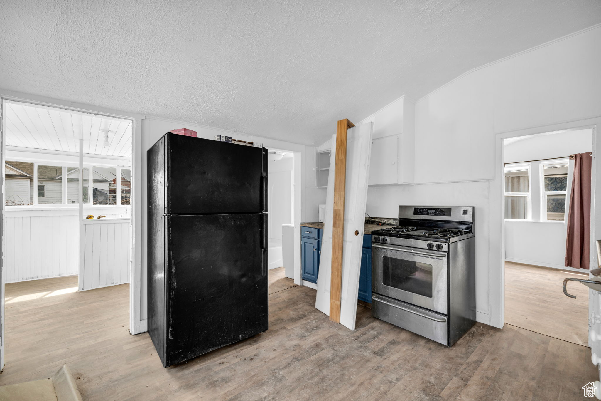 Kitchen with light wood-type flooring, black refrigerator, a wealth of natural light, gas stove, and white cabinets