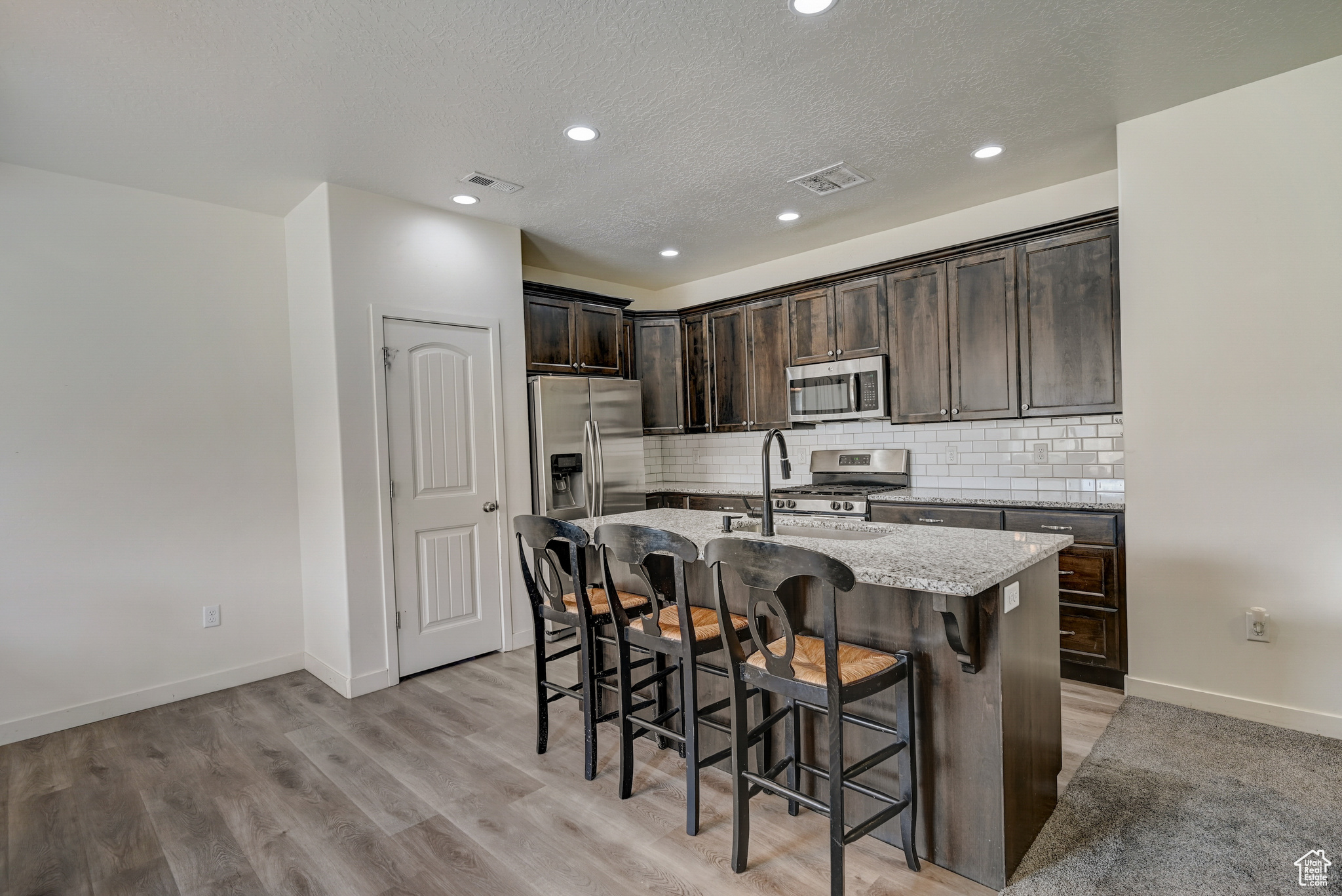 Kitchen with a breakfast bar, light stone counters, a center island with sink, stainless steel appliances, and light LVP flooring