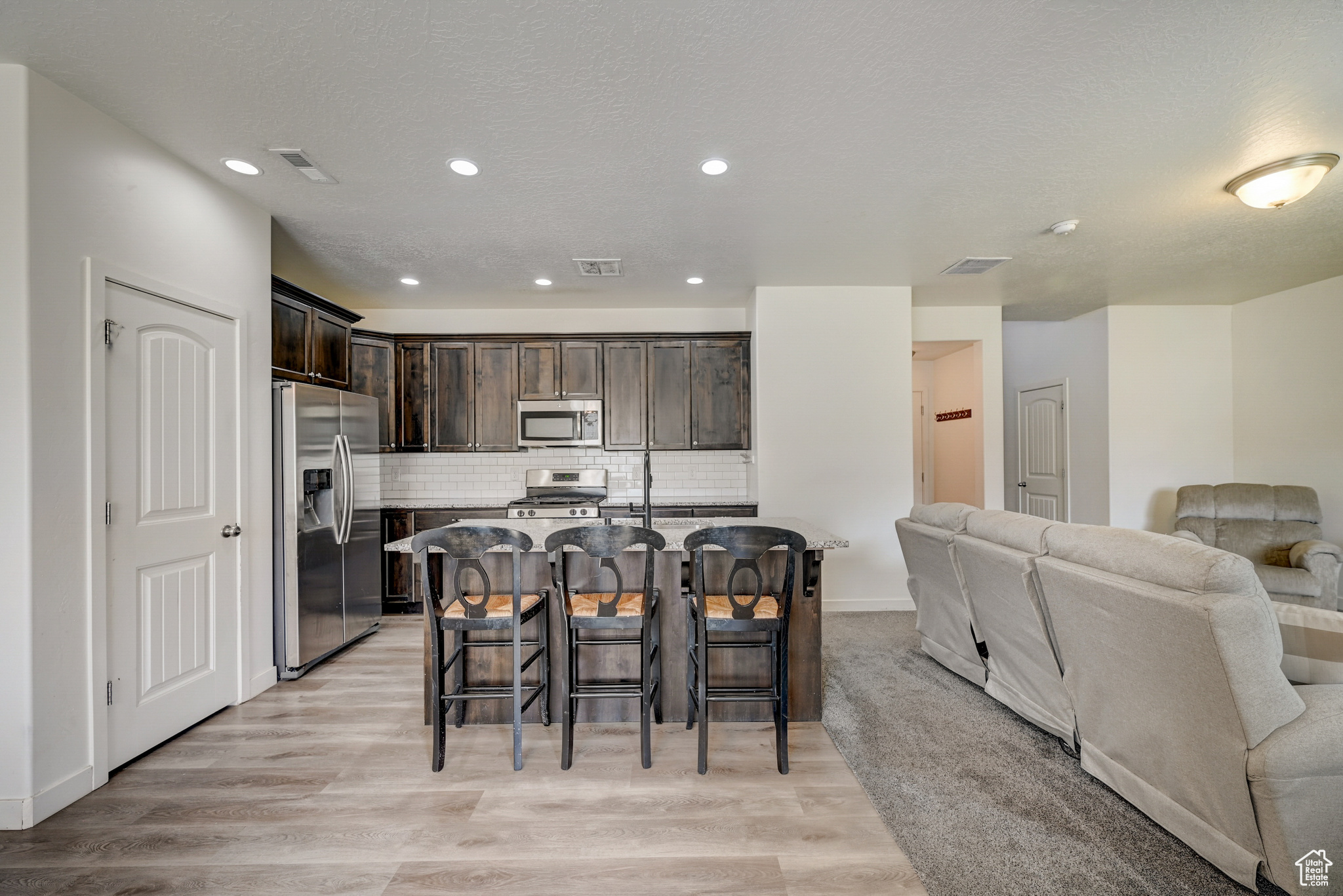 Kitchen with appliances with stainless steel finishes, light wood-type flooring, tasteful backsplash, an island with sink, and a kitchen bar