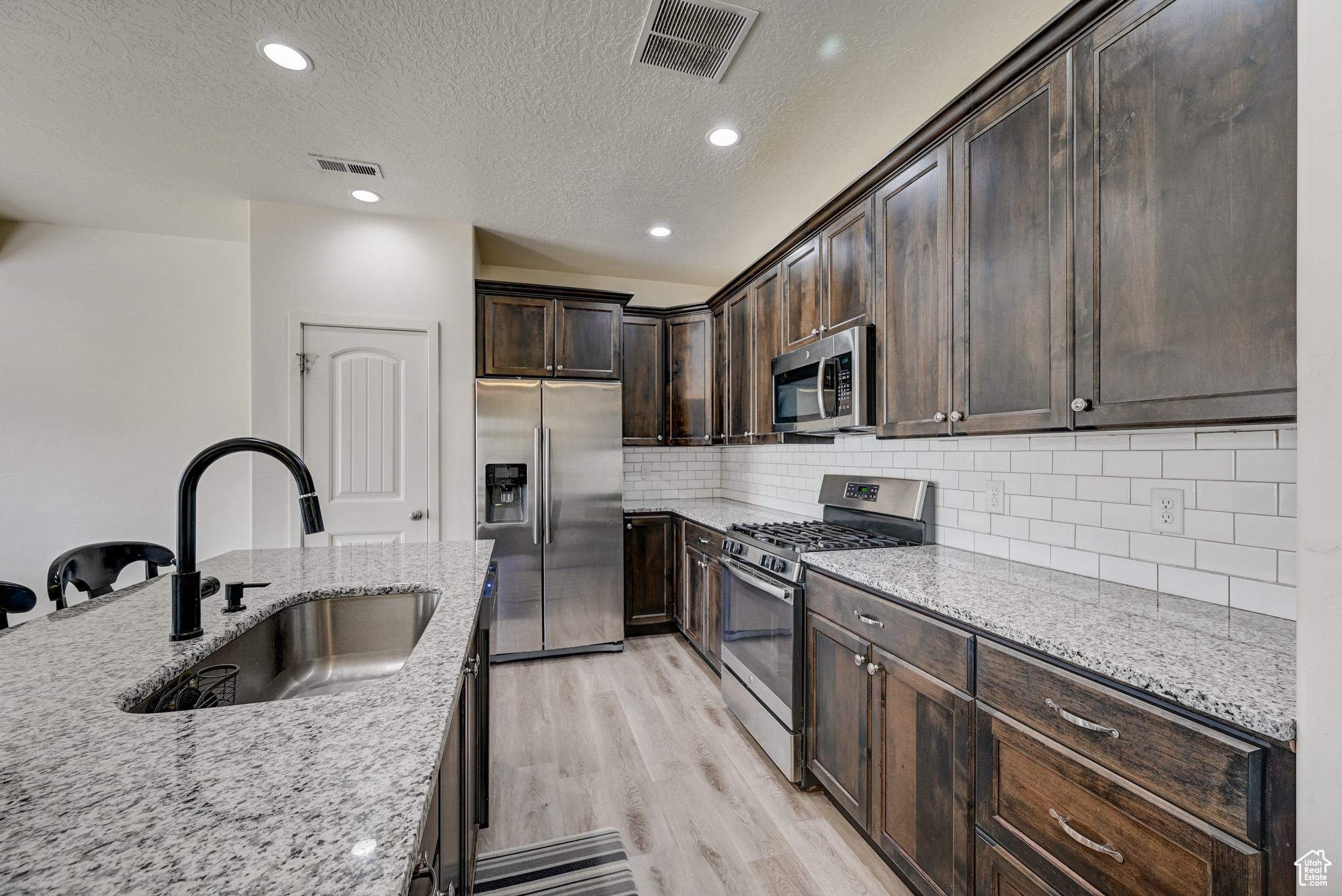 Kitchen featuring light stone counters, light hardwood / wood-style floors, dark brown cabinets, stainless steel appliances, and sink