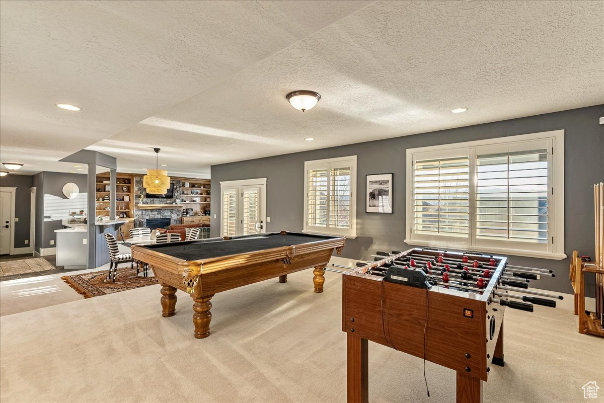 Rec room featuring billiards, a fireplace, a textured ceiling, and light colored carpet