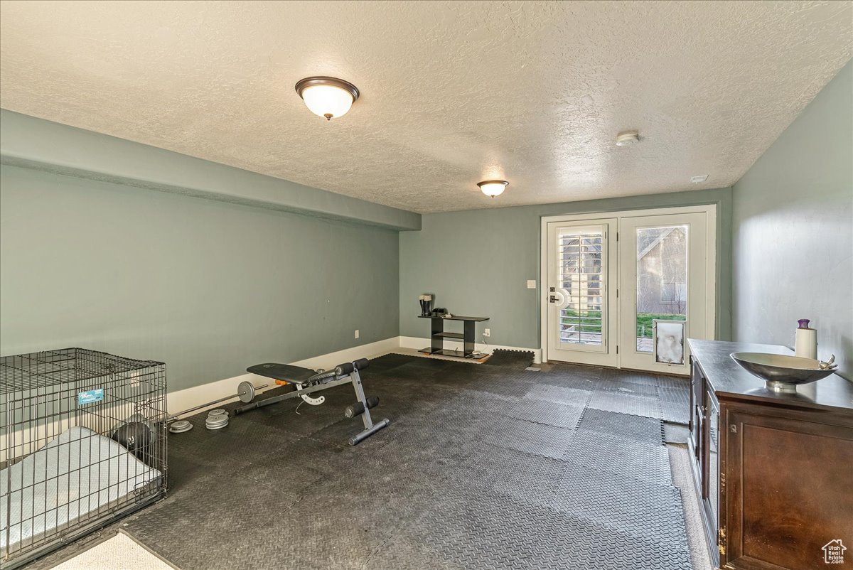 Exercise room featuring french doors, a textured ceiling, and dark carpet