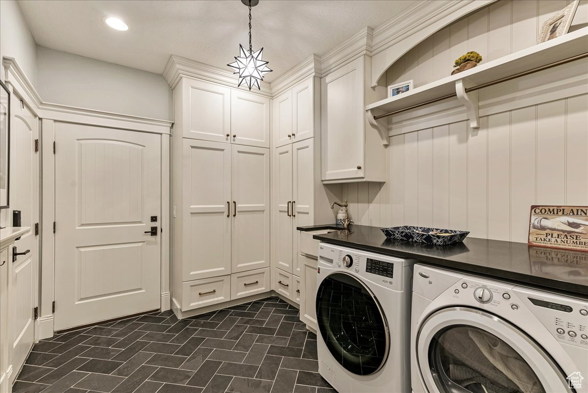 Laundry area featuring dark tile flooring, sink, cabinets, and washer and clothes dryer