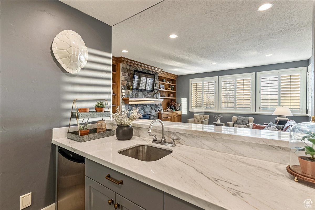 Kitchen with light stone counters, gray cabinetry, dishwasher, a textured ceiling, and sink