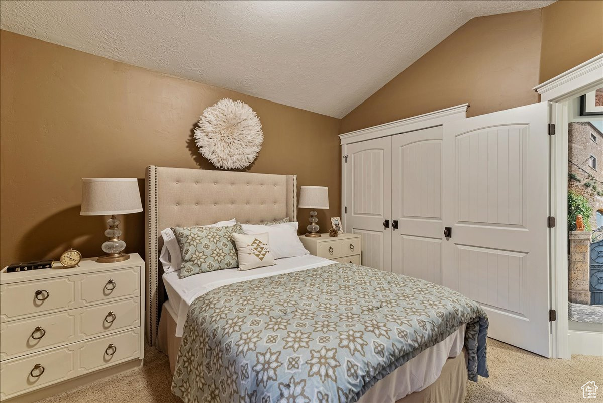 Bedroom with light colored carpet, vaulted ceiling, and a textured ceiling