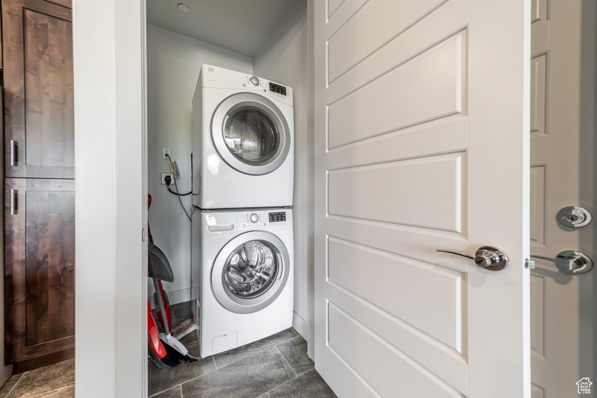 Laundry room featuring electric dryer hookup, dark tile floors, and stacked washer and clothes dryer