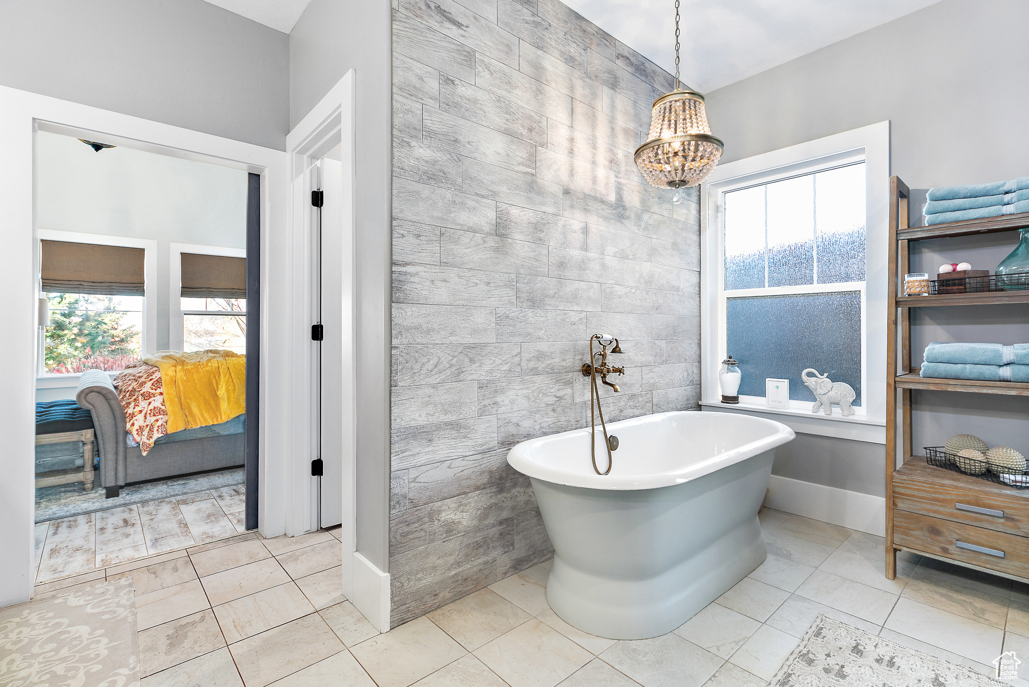 Primary Bathroom featuring tile walls, a bath to relax in, tile floors, and an inviting chandelier