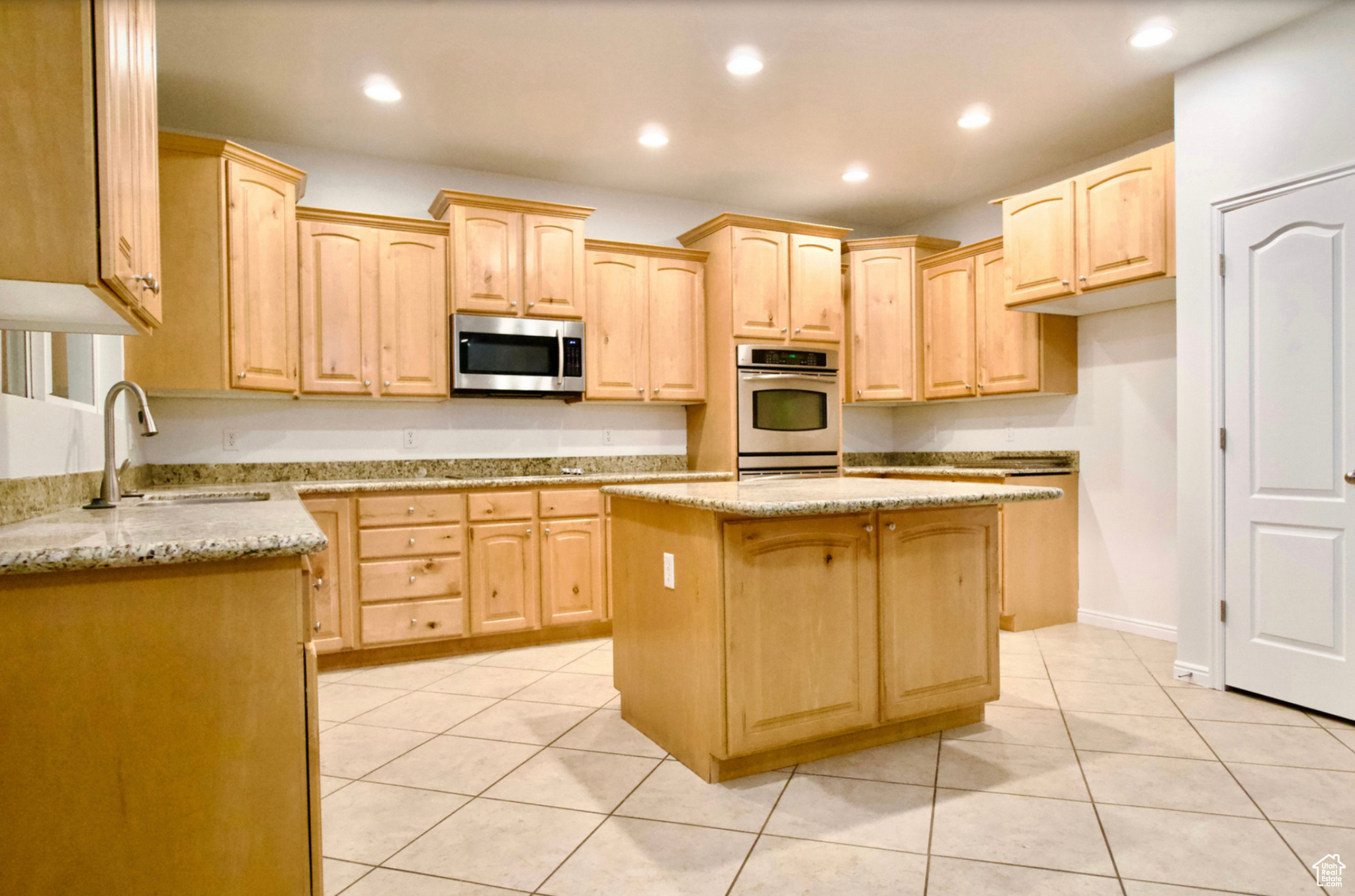Kitchen with light tile floors, stainless steel appliances, sink, light stone countertops, and a kitchen island