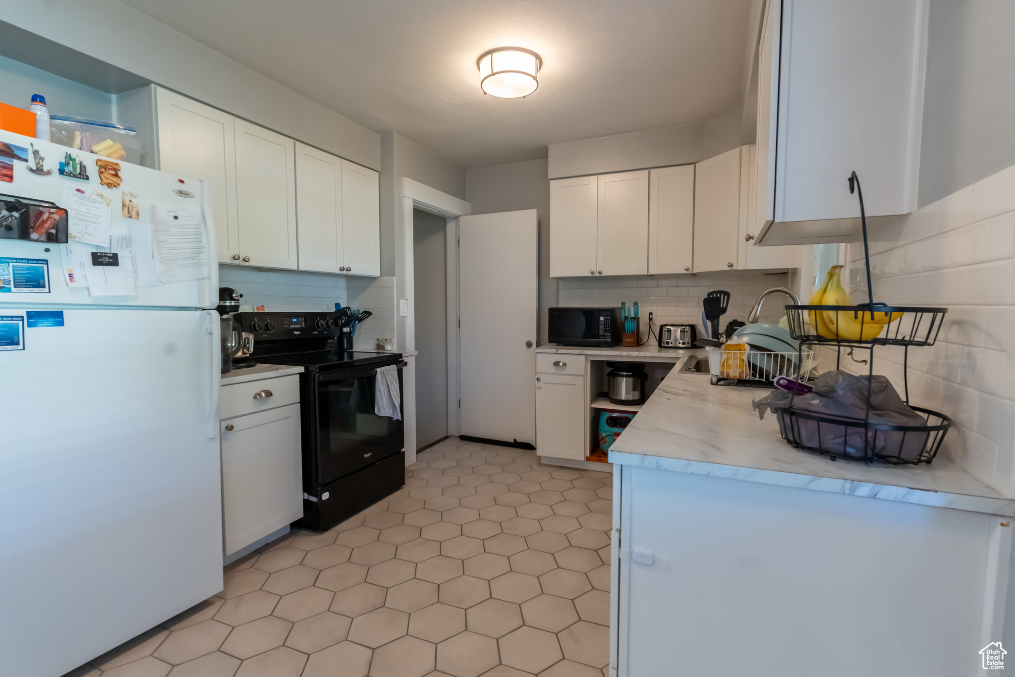 Kitchen with tasteful backsplash, white cabinets, black appliances, and light tile flooring