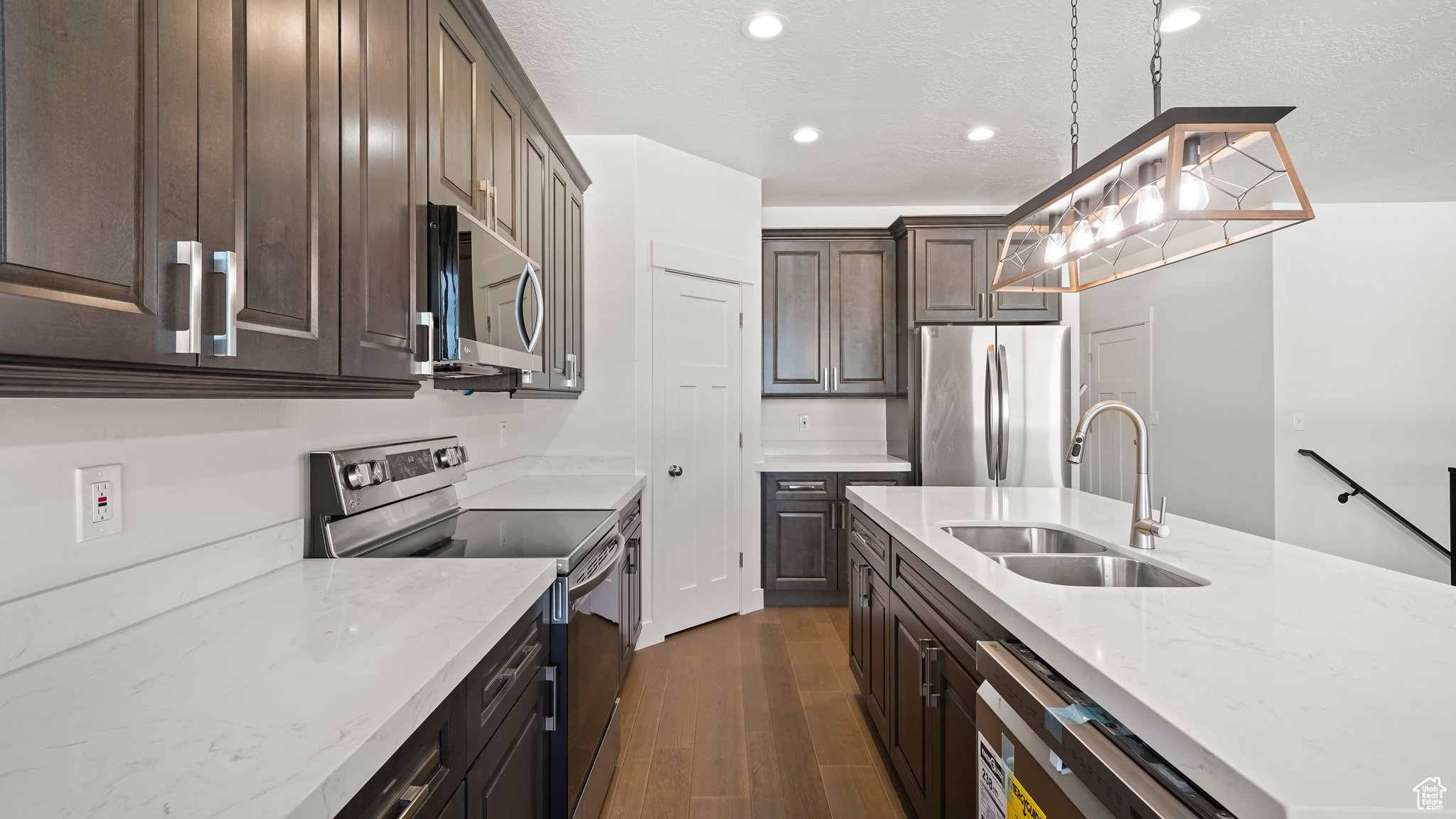 Kitchen with light stone countertops, dark wood-type flooring, stainless steel appliances, decorative light fixtures, and sink